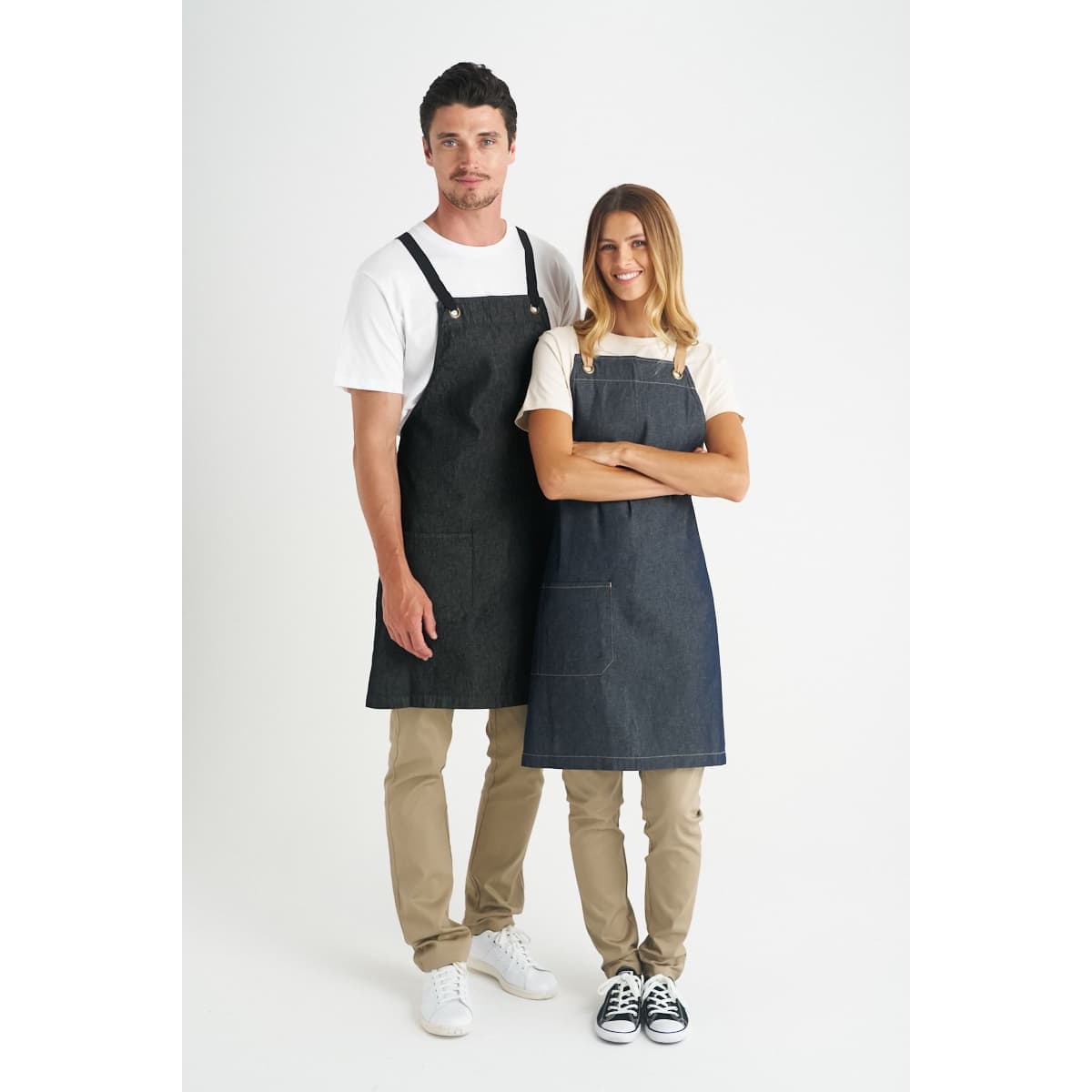A pair of denim bib aprons in dark blue, worn by a man and a woman, featuring adjustable straps and pockets.