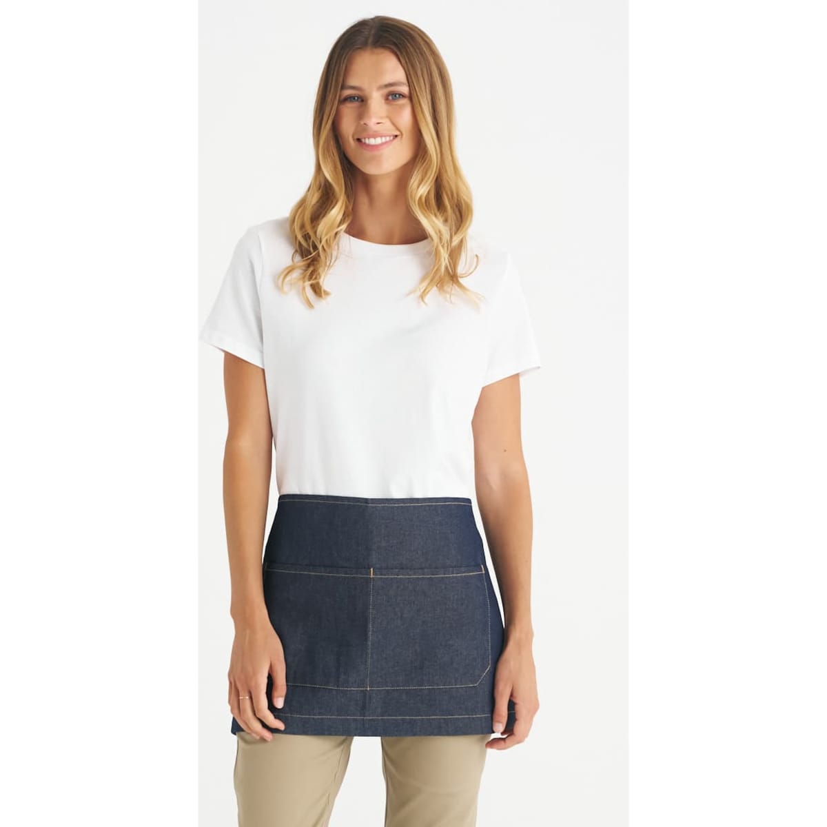 A woman in a white t-shirt wears a dark denim short waist apron. The apron features stitching details and a logo.