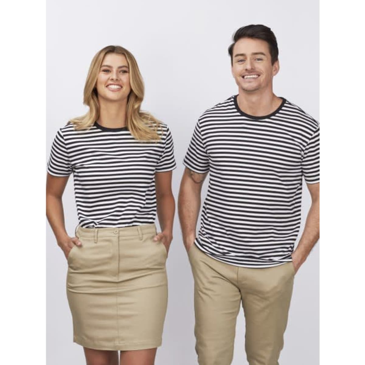 A striped black and white unisex T-shirt displayed on two models, one male and one female, paired with beige bottoms.