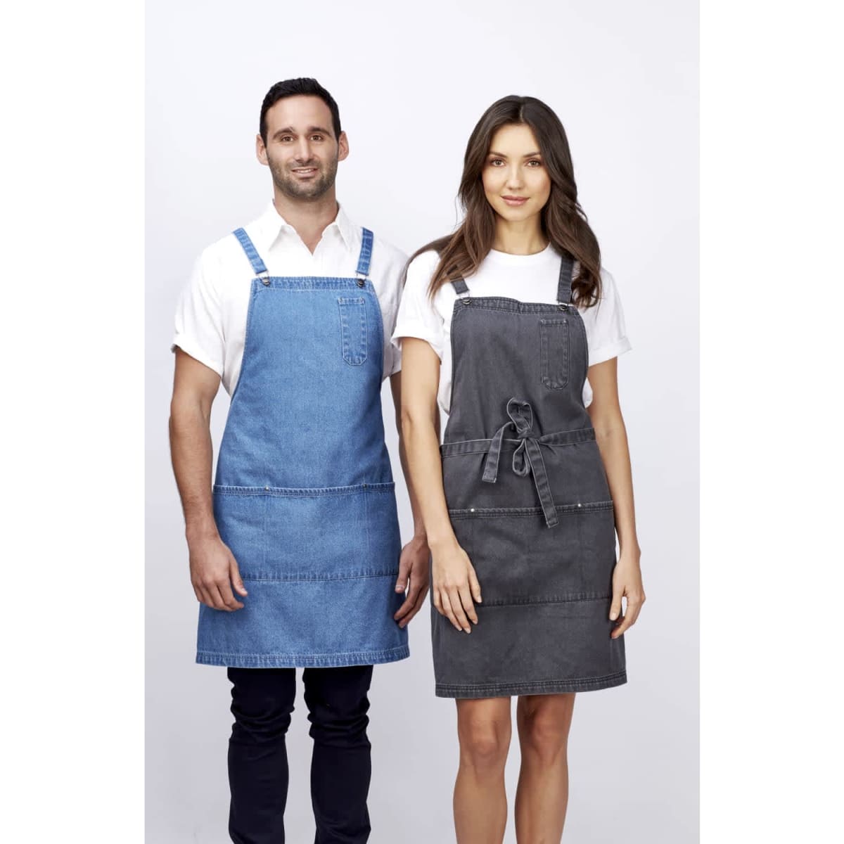 A denim bib apron in blue on a man and a grey apron on a woman, both featuring pockets and ties.