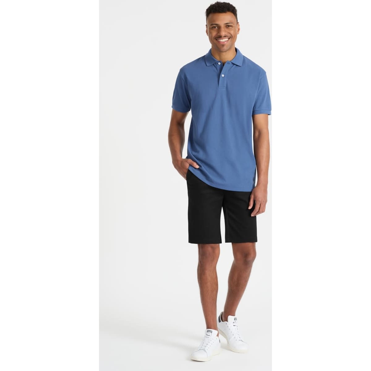 A man wearing a blue polo shirt and black shorts, paired with white sneakers. The shirt features a logo.
