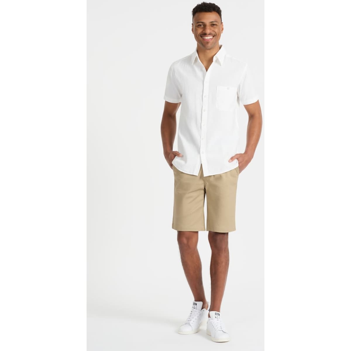 A model wearing beige chino shorts and a white short-sleeved shirt, paired with white sneakers. Logo visible.