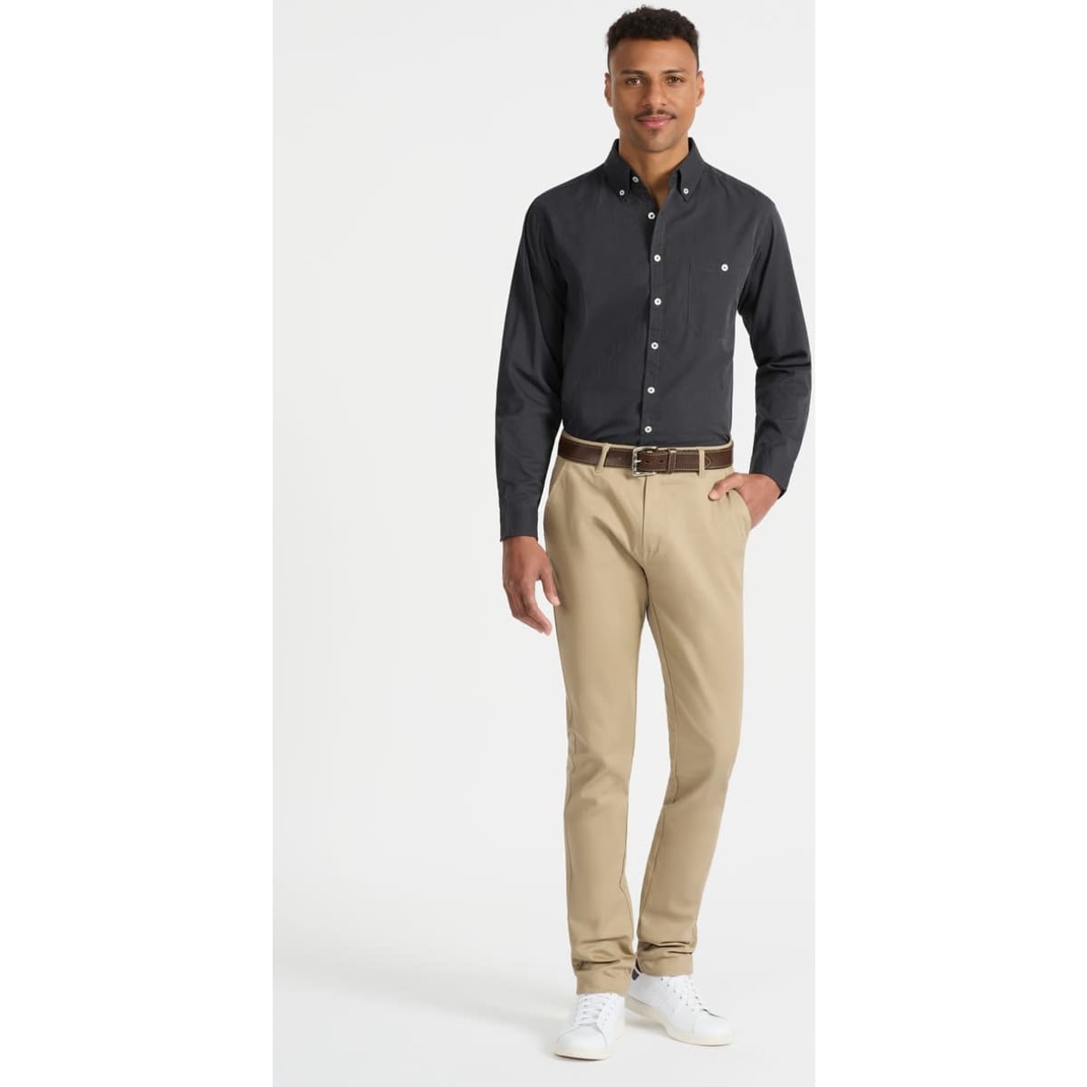 A model wearing a black long sleeve button-up shirt paired with beige trousers and white shoes, featuring a small logo.