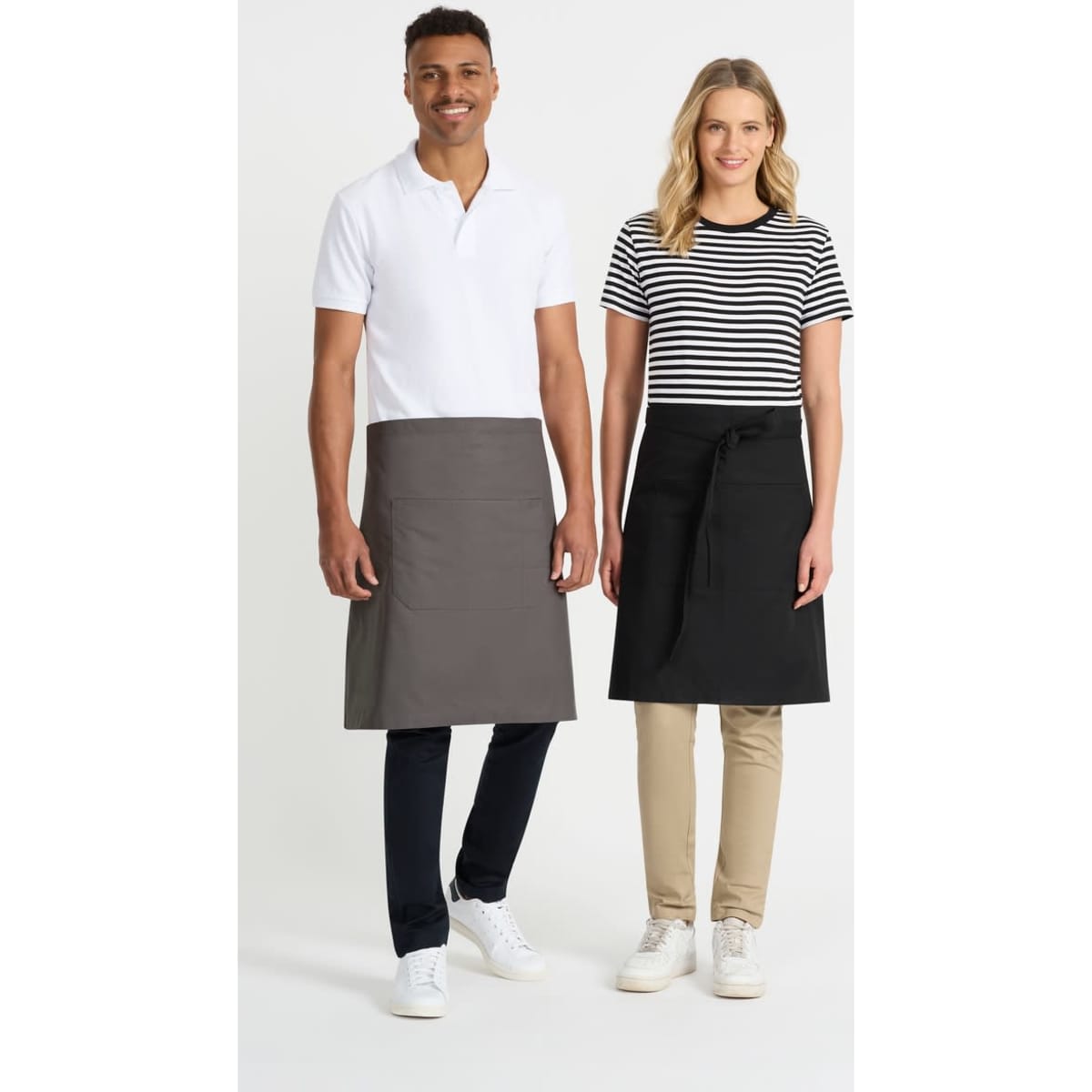Two models wearing aprons, one in grey and the other in black, standing side by side. Both models are dressed in casual attire.