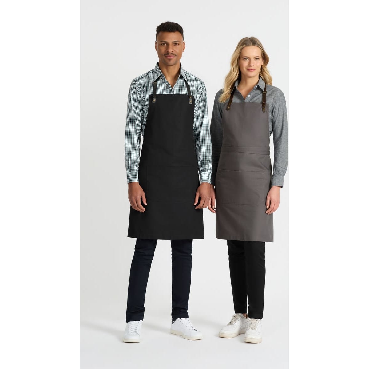 A black and a grey bib apron are displayed on two models, with each wearing a collared shirt and pants.