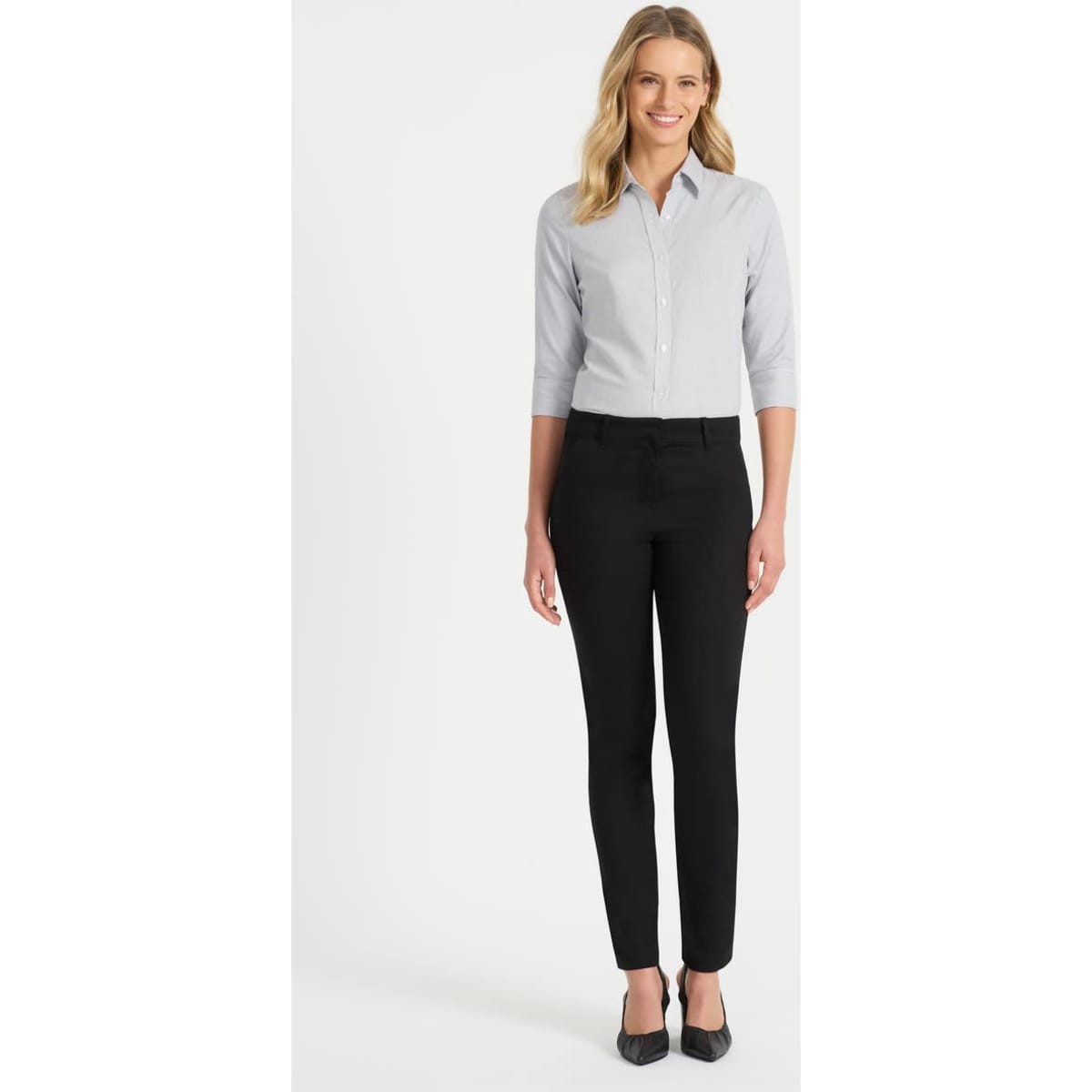 A woman is wearing a grey button-up shirt with 3/4 sleeves and black trousers, standing on a plain background.