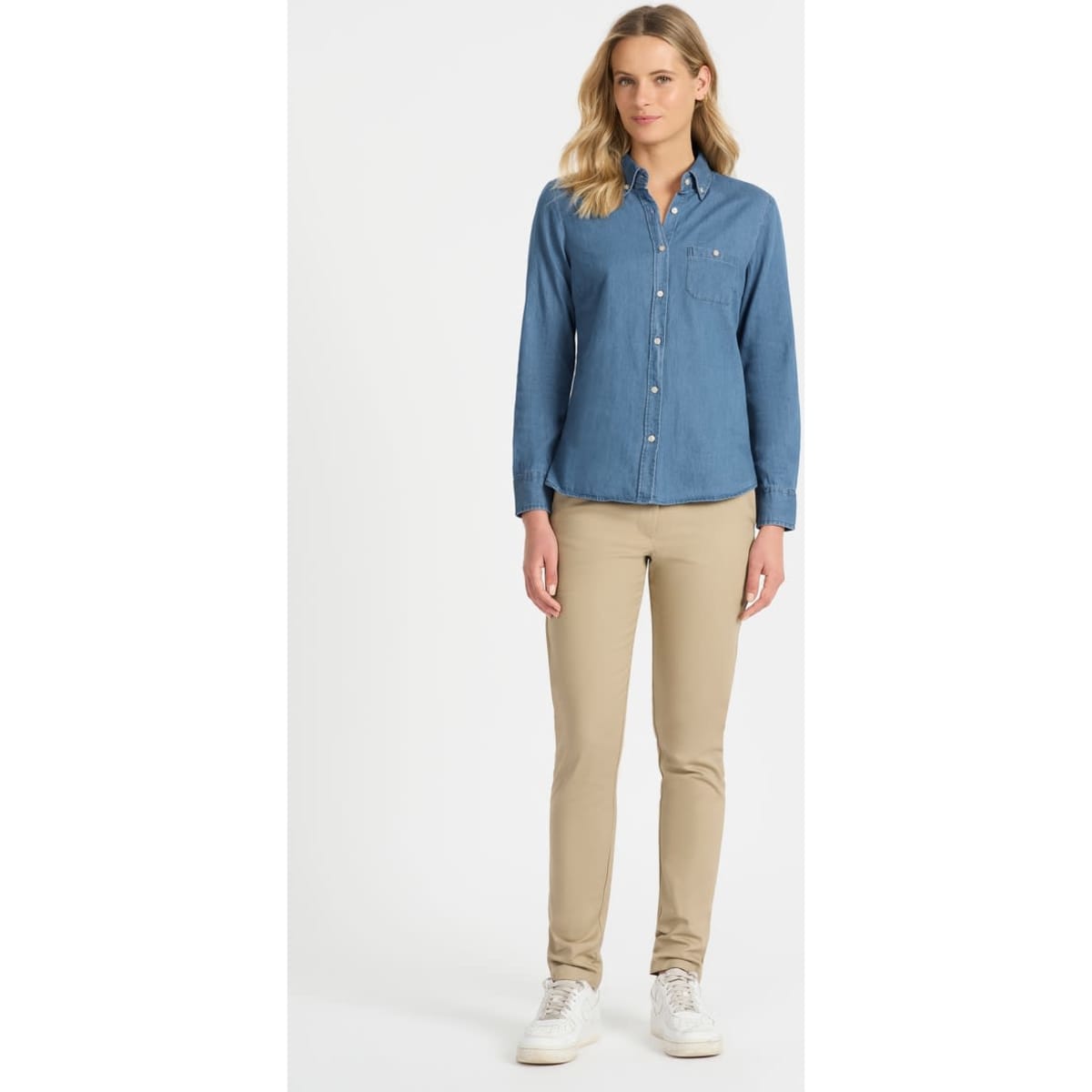 A ladies' long sleeve button-up shirt in denim blue, paired with beige trousers and white sneakers. The shirt has a chest pocket and branding.