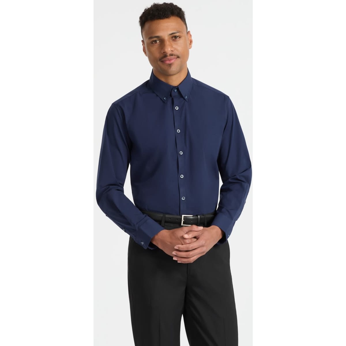 A men's long sleeve button-up shirt in navy blue, featuring a collar and buttons down the front, worn with black trousers.