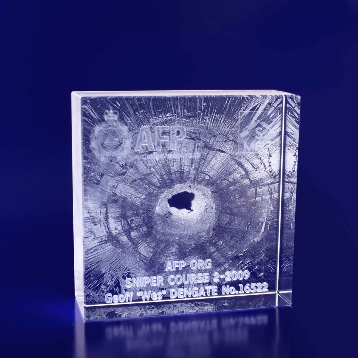 A clear 3D crystal square, 100x100x35mm, featuring a round hole and a logo. The surface has textured detail.