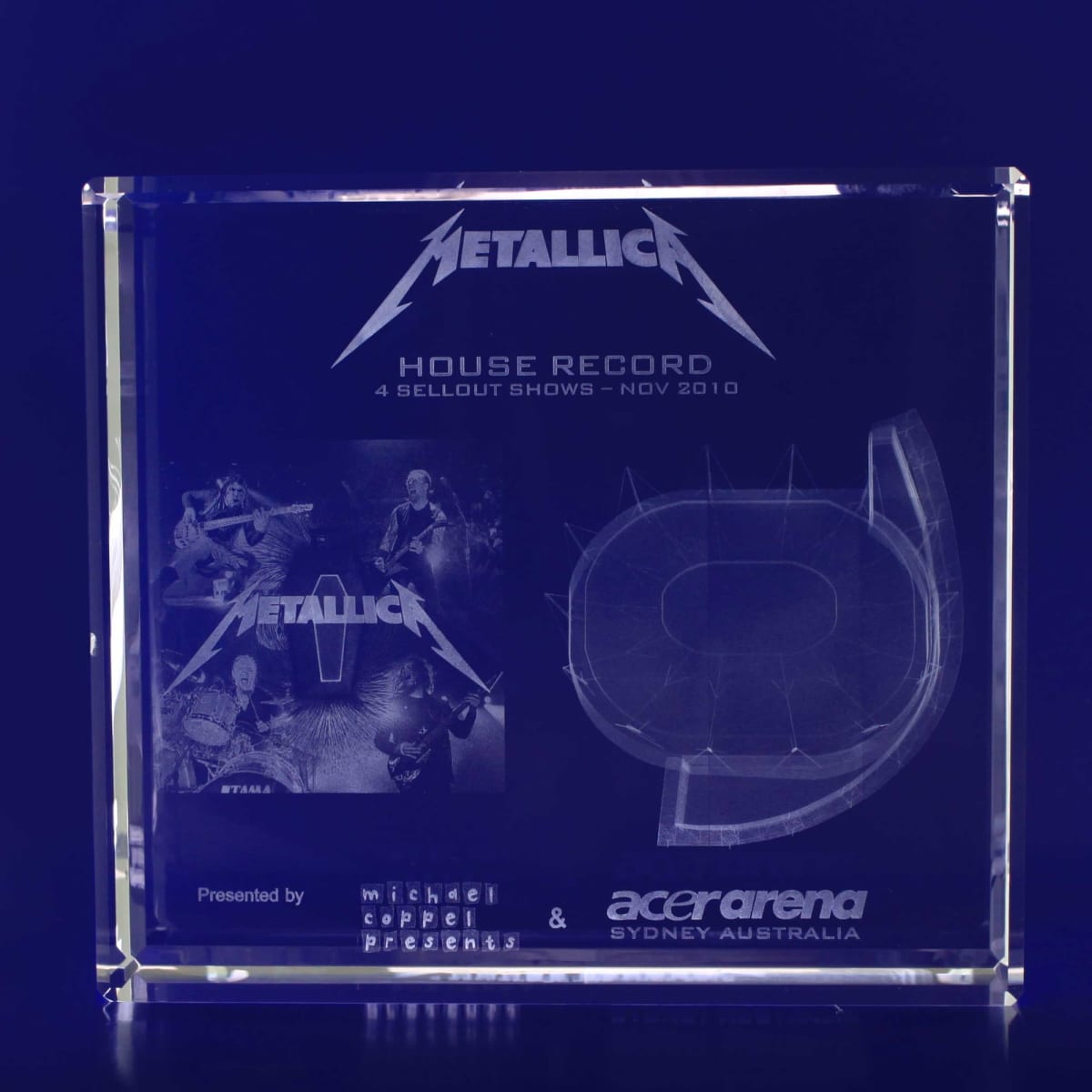 A clear 3D crystal square featuring an engraved Metallica design and logo, with images and a stadium outline.