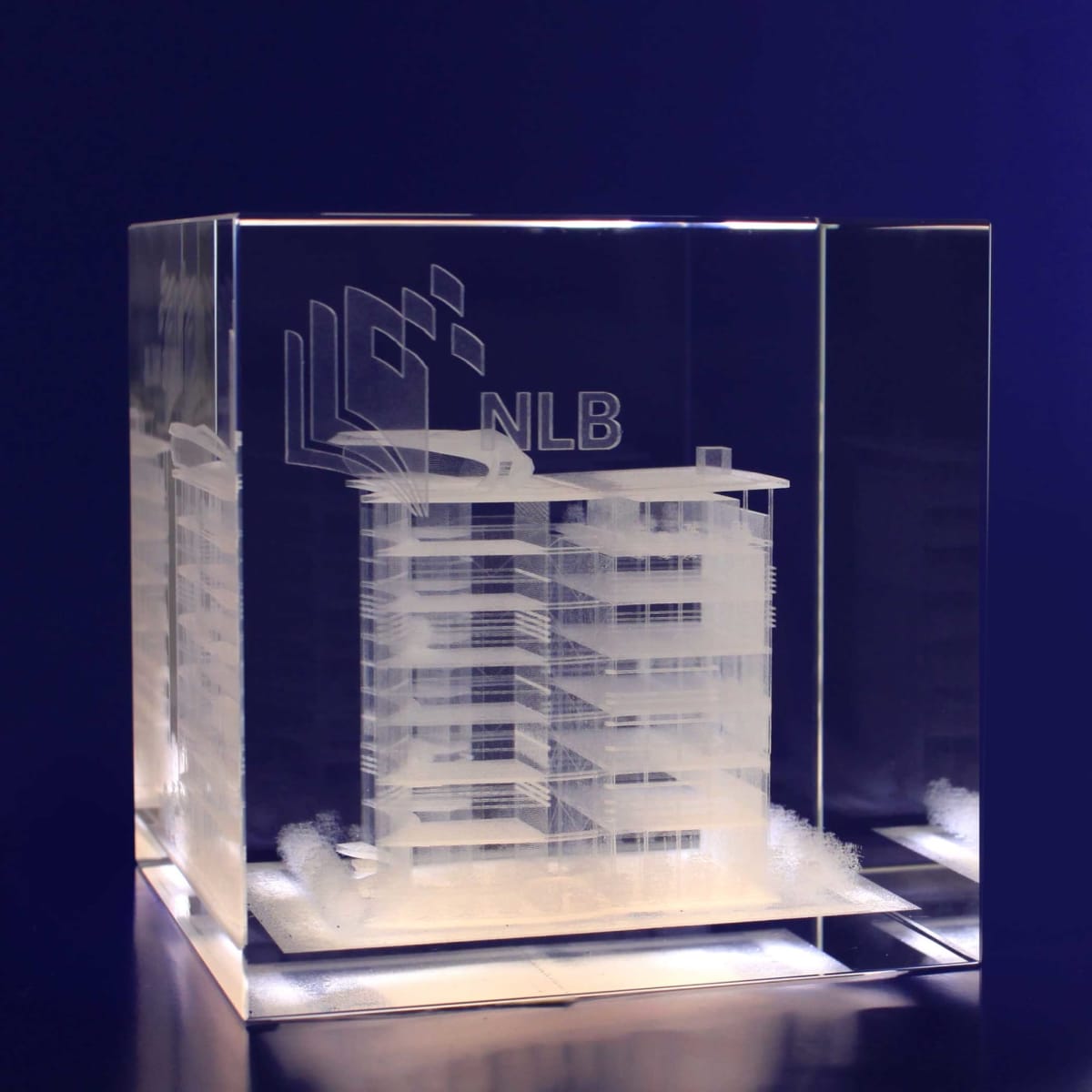 A 3D crystal cube, 100mm, features an engraved building design and has a clear, glass-like appearance.