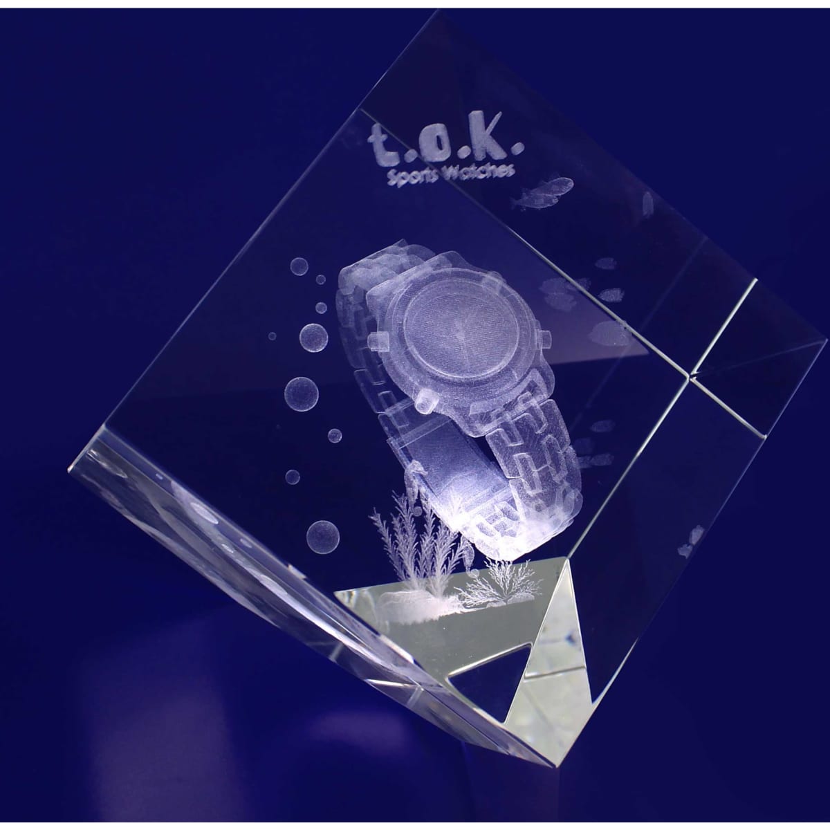 A clear 3D crystal diamond showcasing a detailed optical engraving of a sports watch, with a brand logo and bubbles.