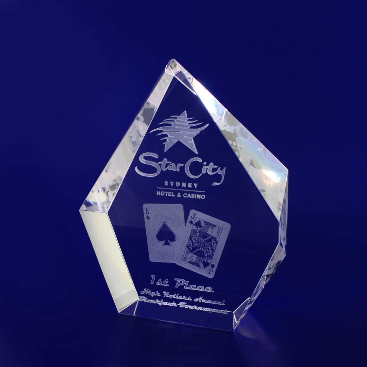 A transparent crystal trophy in a diamond shape, featuring playing card motifs and a logo.