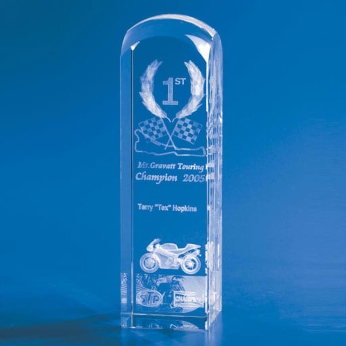 A clear crystal trophy with a dome top, featuring an engraved design and a reflective base.