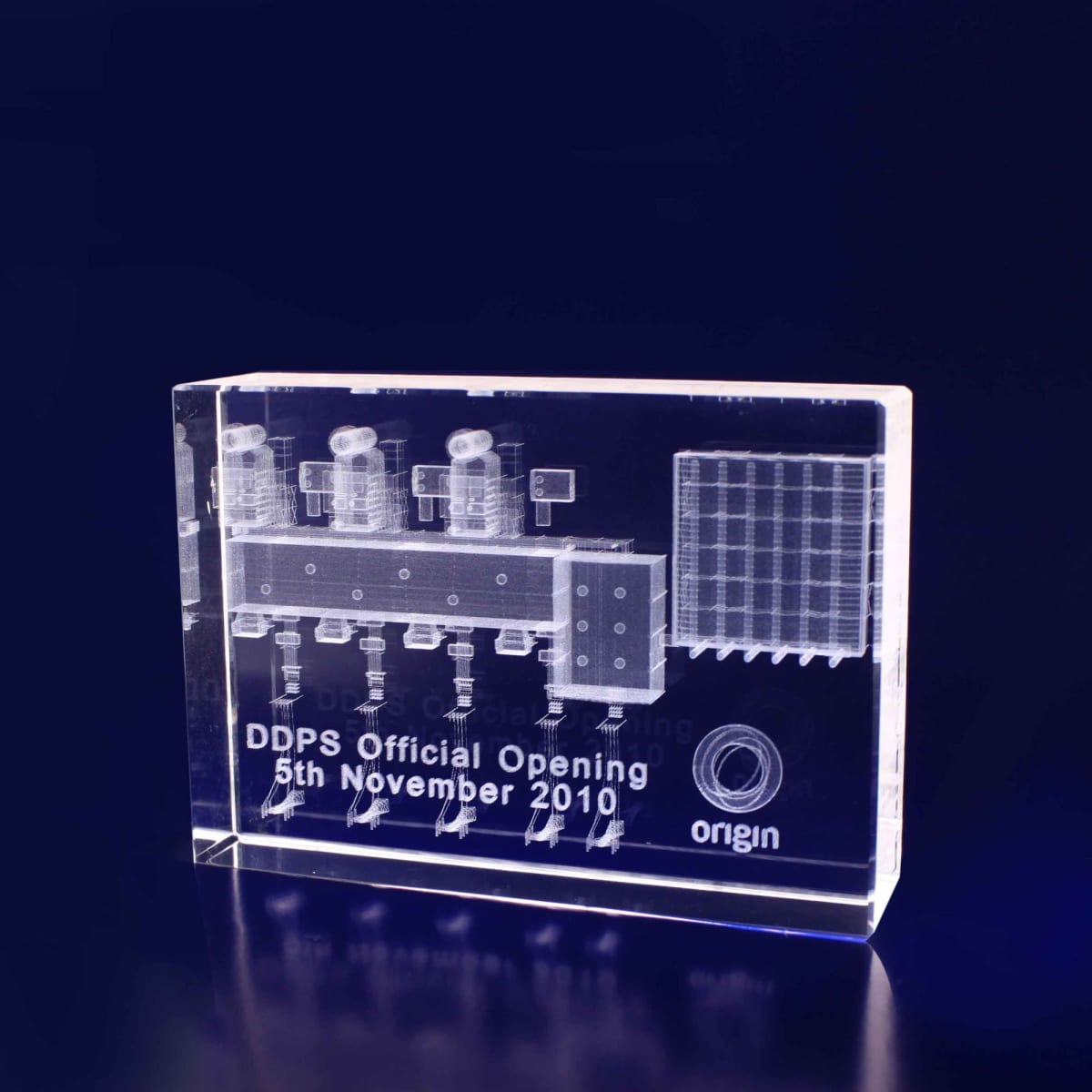 A transparent crystal rectangular block with engraved designs, featuring a logo and text, set against a dark background.