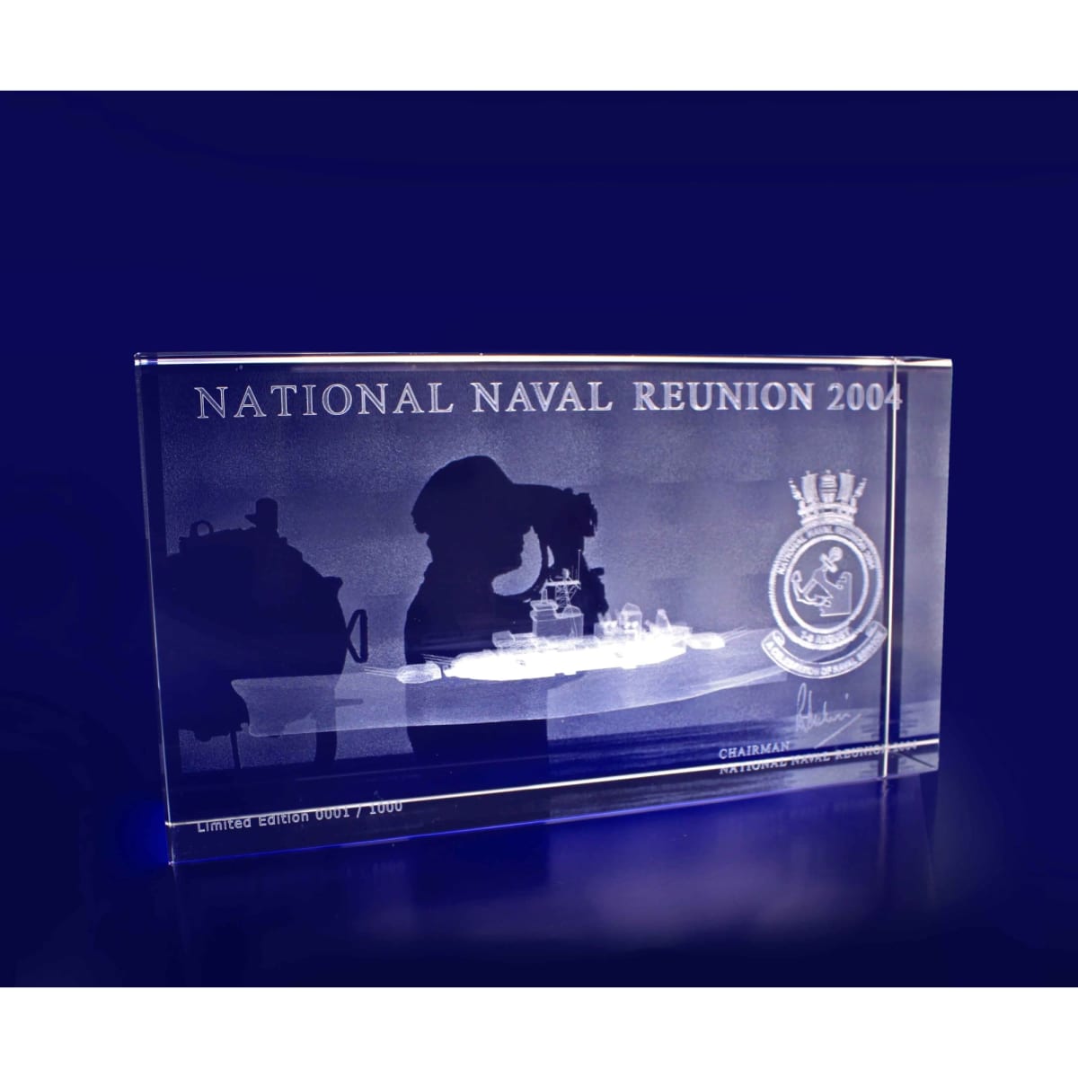 A clear crystal rectangle featuring an etched design, with details and a logo, on a blue background.