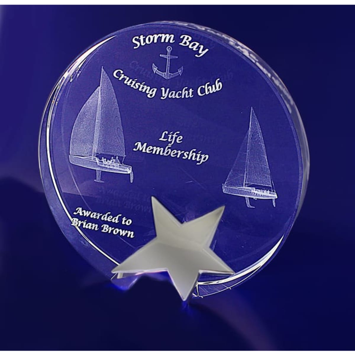 A 3D crystal star award in a round shape, featuring a sailboat design and engraved text, displayed on a blue background.