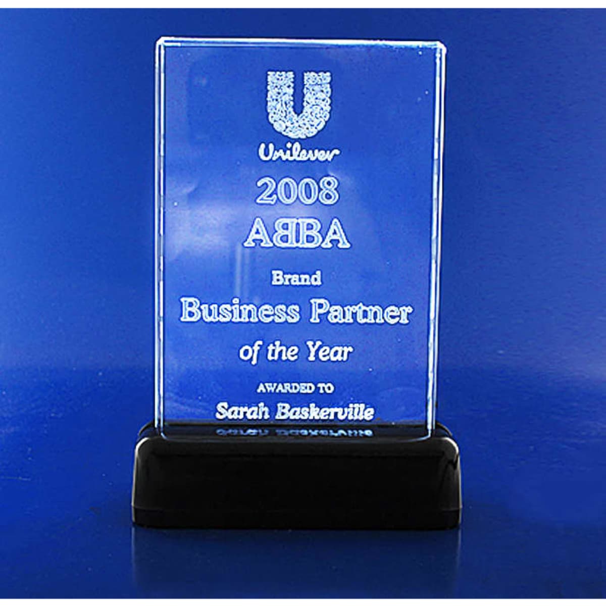 A clear 3D crystal plaque on a black base, featuring a logo and inscriptions celebrating a business award.