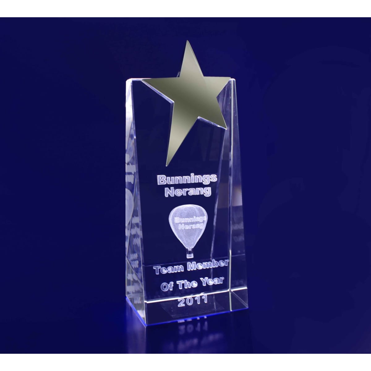 A clear crystal award in a wedge shape, featuring a gold star on top and engraving on the front.
