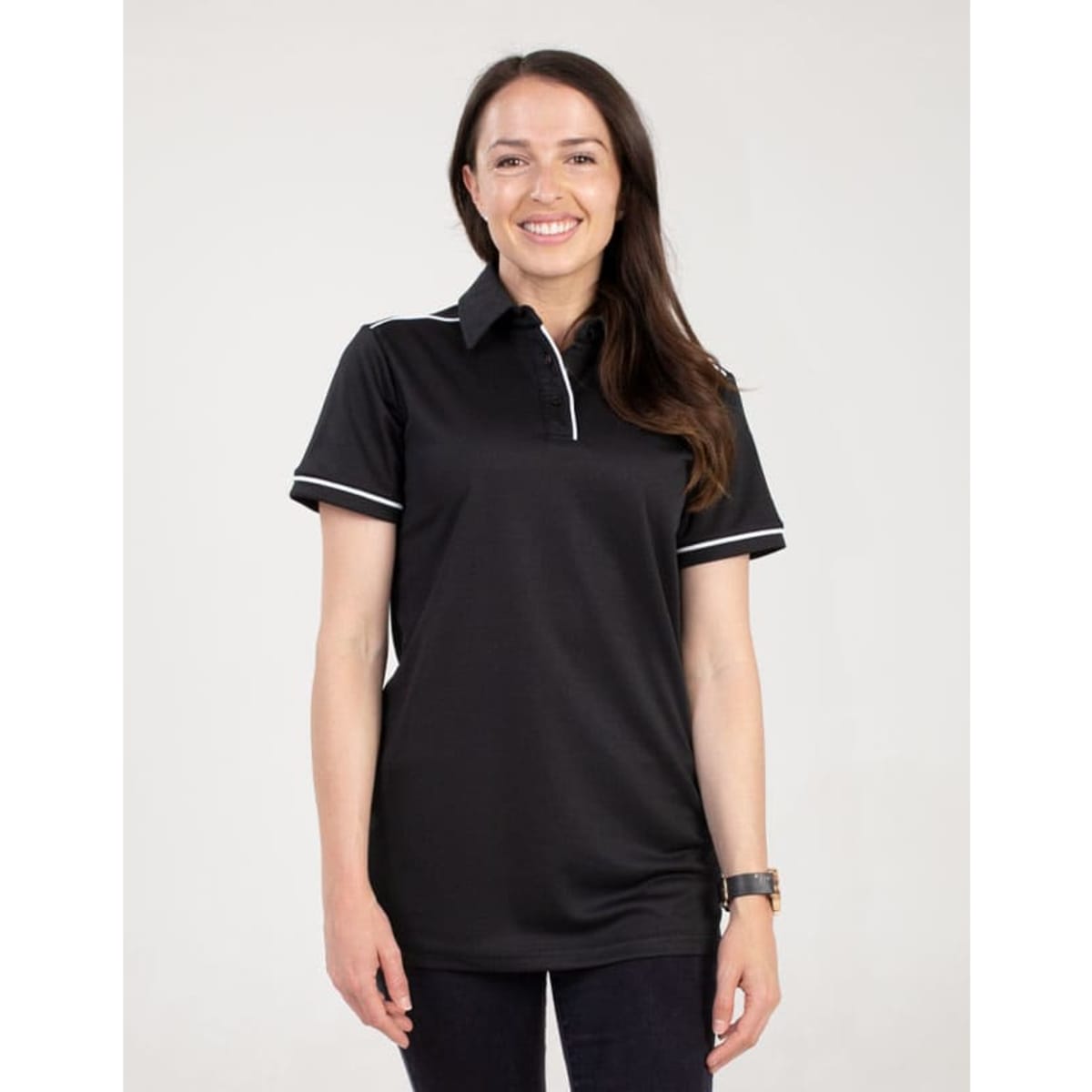 A black polo shirt featuring a collar and contrasting piping, displayed on a smiling woman. The shirt has a logo.