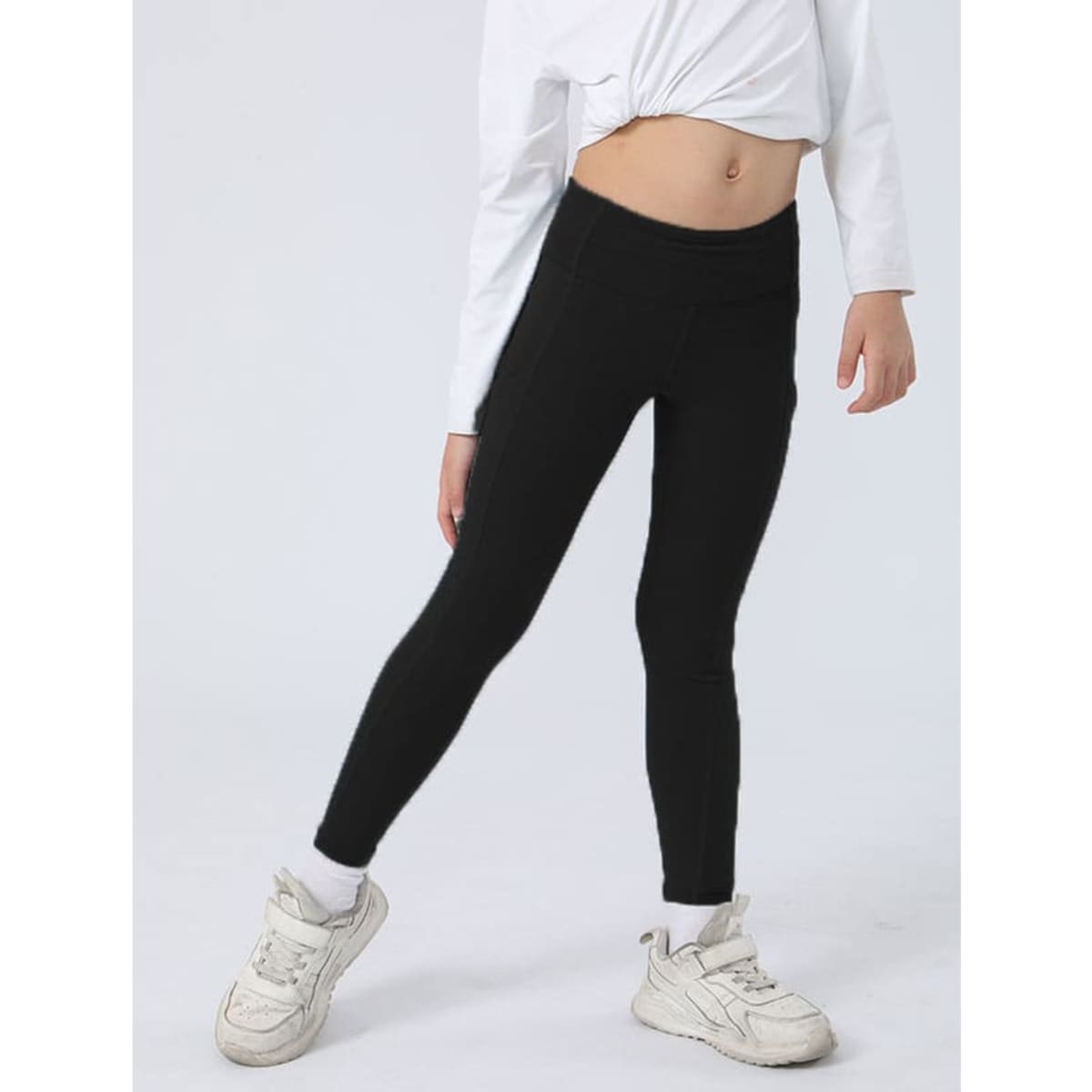 Black leggings worn by a child, paired with a white top and white trainers. The leggings have a fitted design.