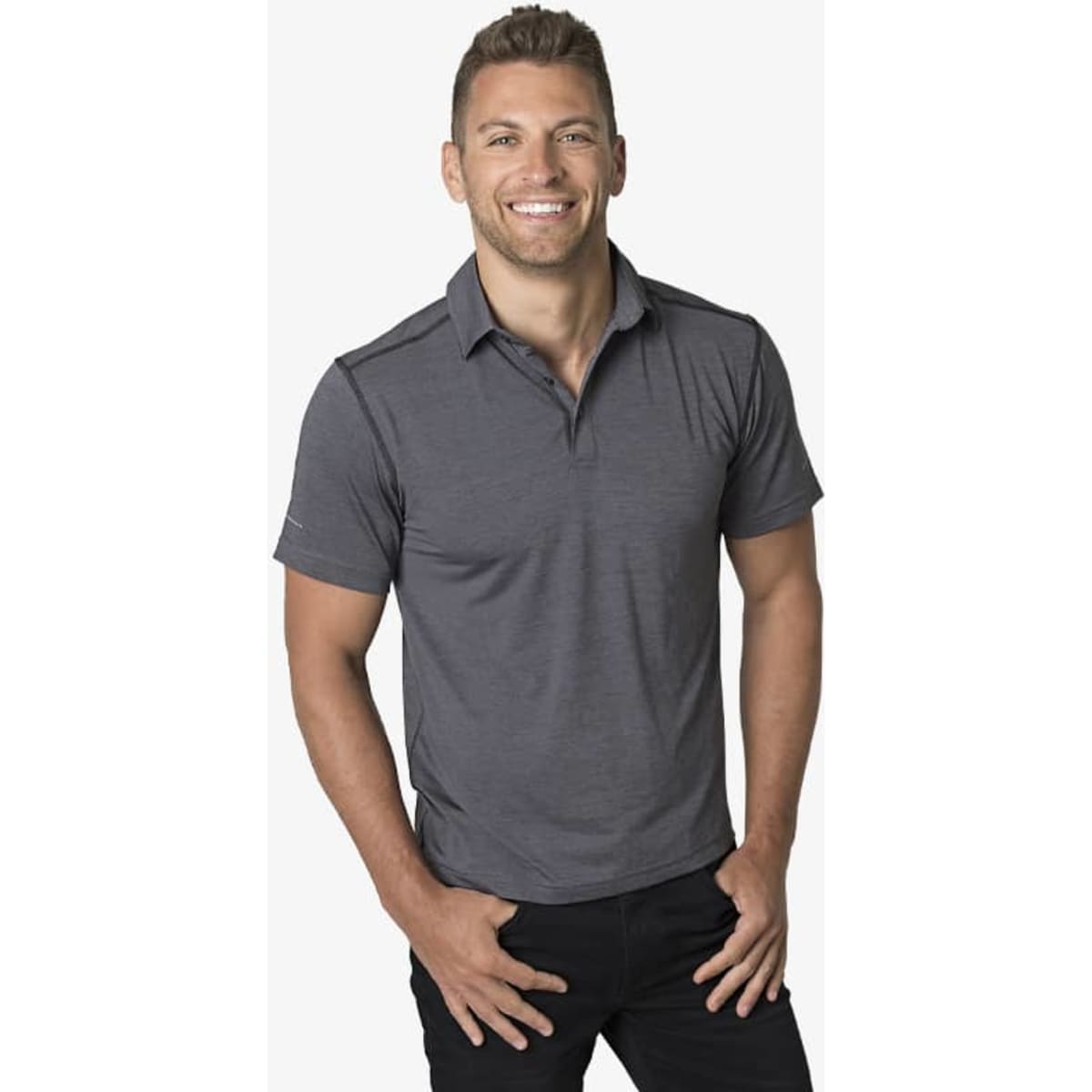 A man smiling, wearing a grey polo shirt, with a relaxed fit and short sleeves. It features a logo.