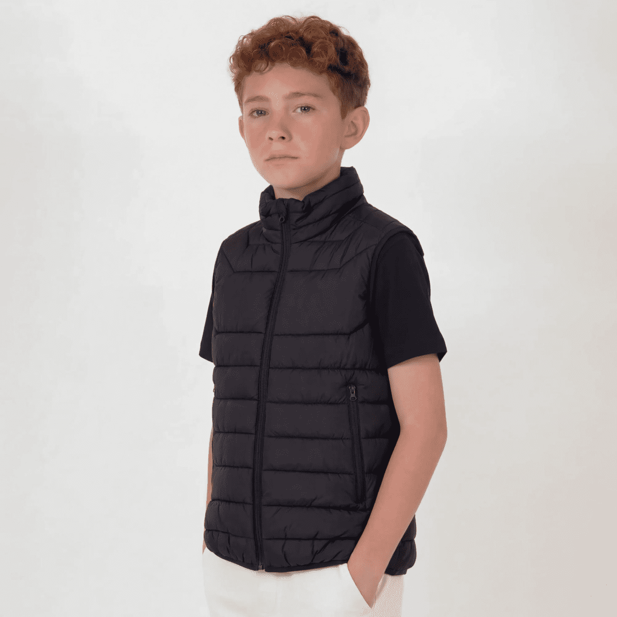 A youth puffer vest in black, featuring a zip-up front and high collar, worn by a young boy against a neutral background.