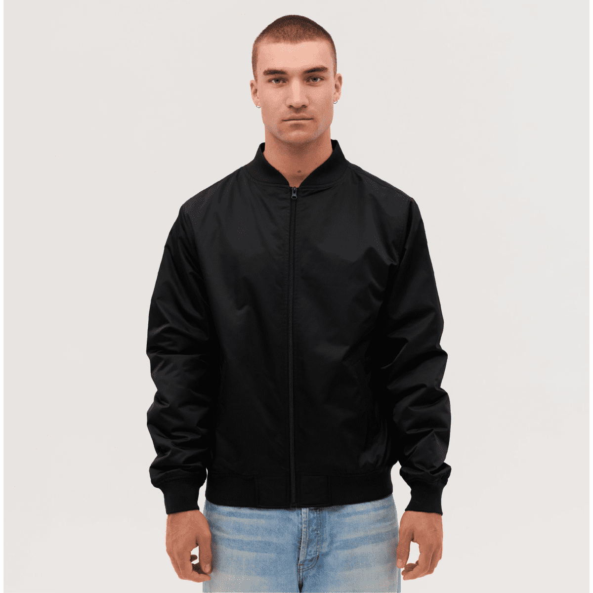 A black bomber jacket worn by a model, featuring a zip front and ribbed cuffs. The model has short hair and is standing against a neutral background.