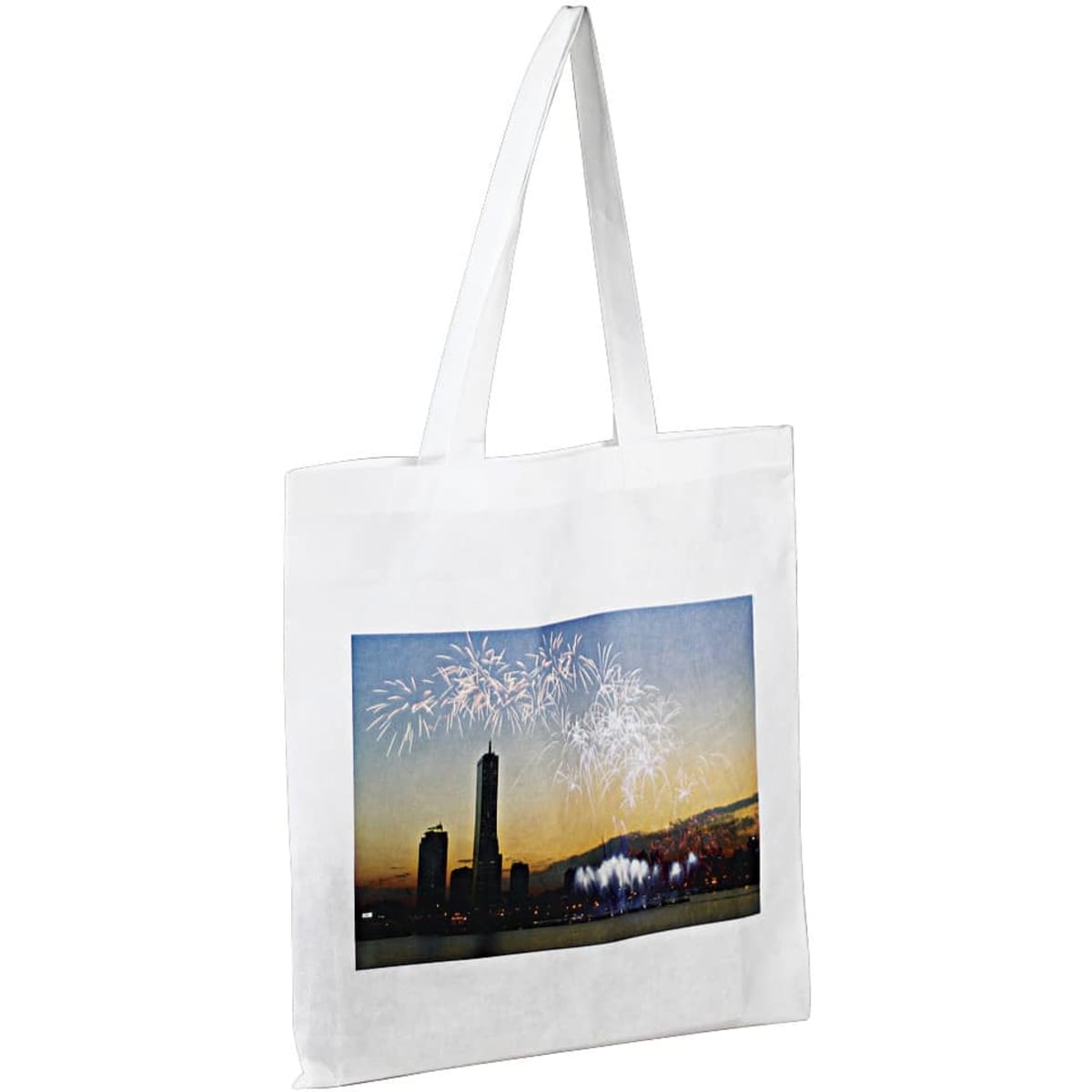A white tote bag featuring a printed image of a city skyline with fireworks in the background. It has long handles.