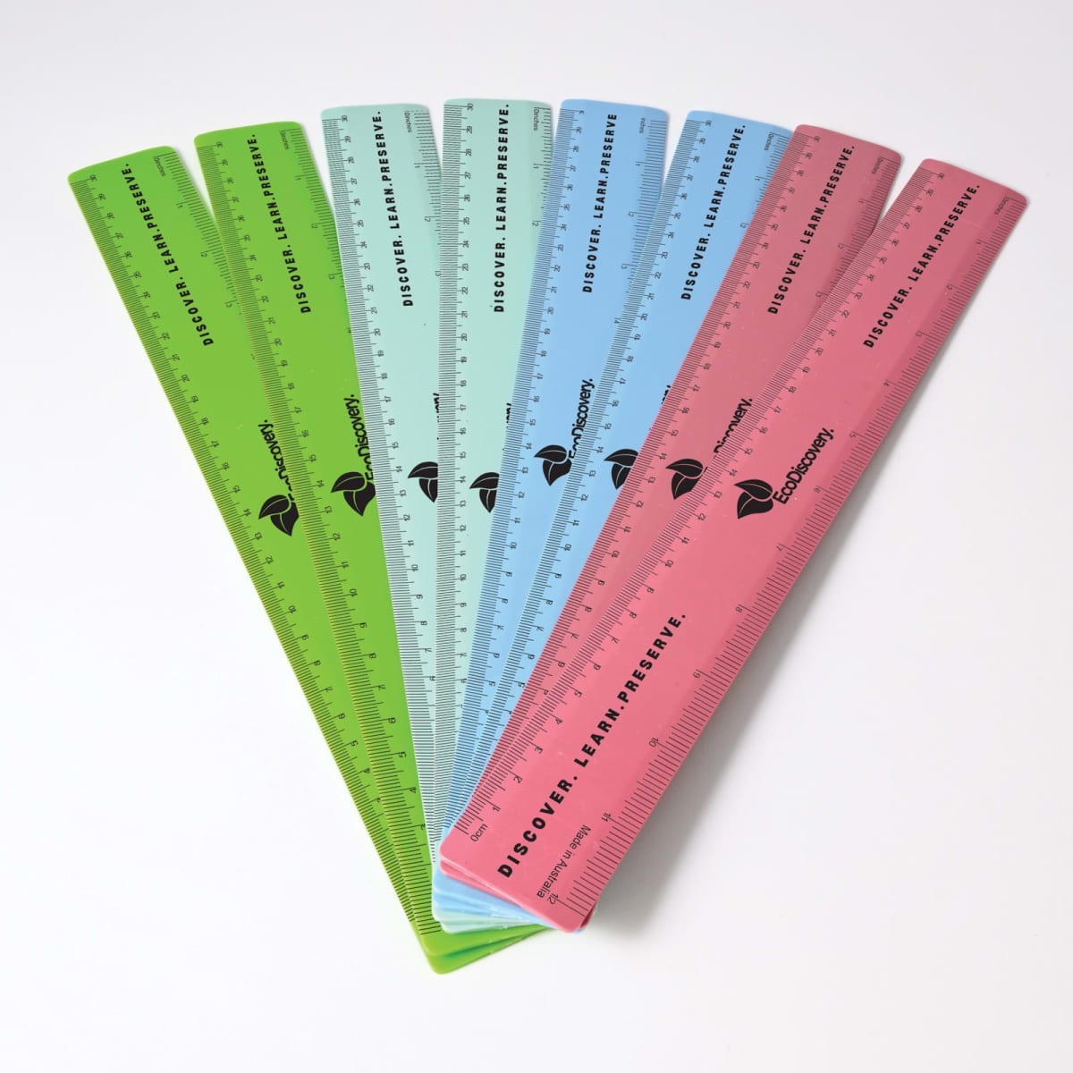 A collection of recycled plastic rulers in green, blue, and pink, featuring a logo and measurement markings.