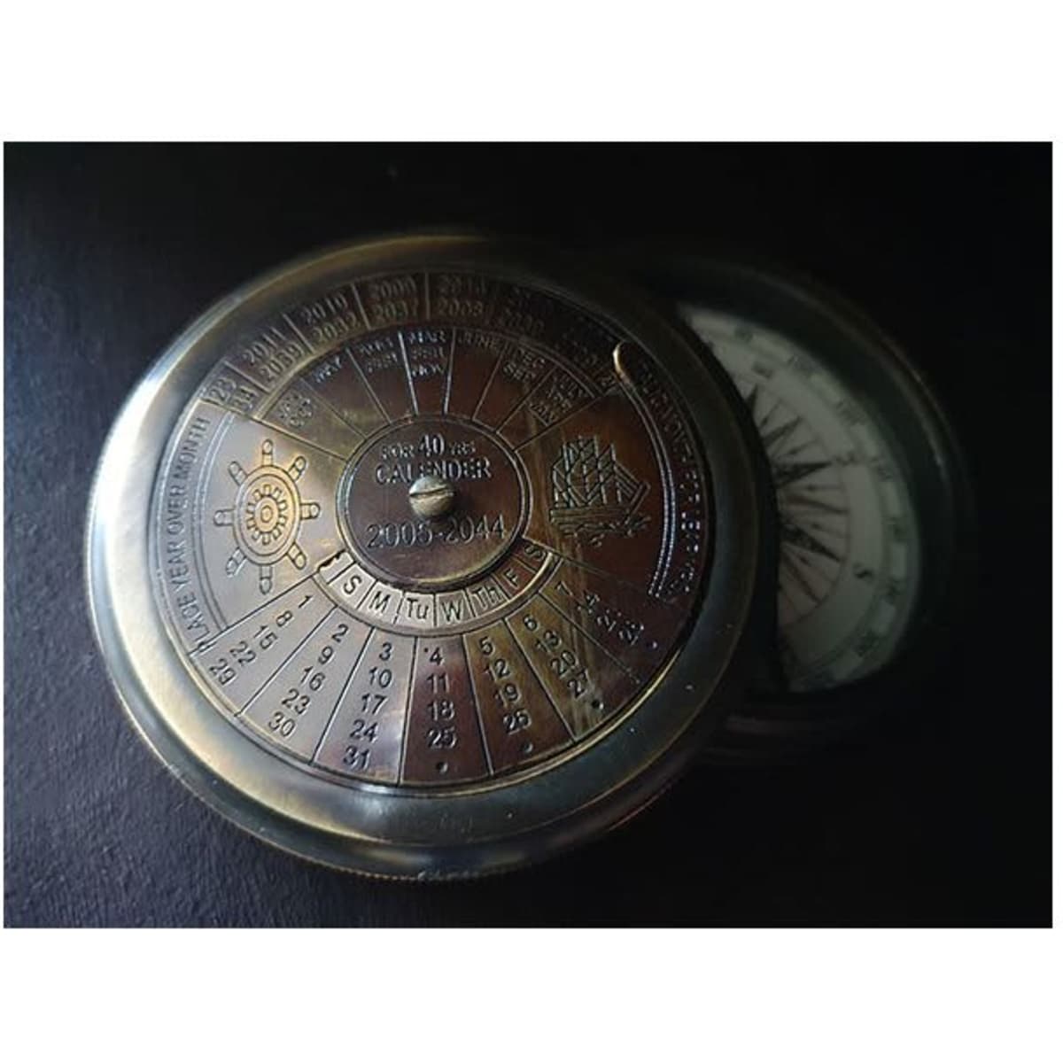 A silver magnetic compass and calendar, featuring a detailed dial with numbers and symbols, with a reflective finish.