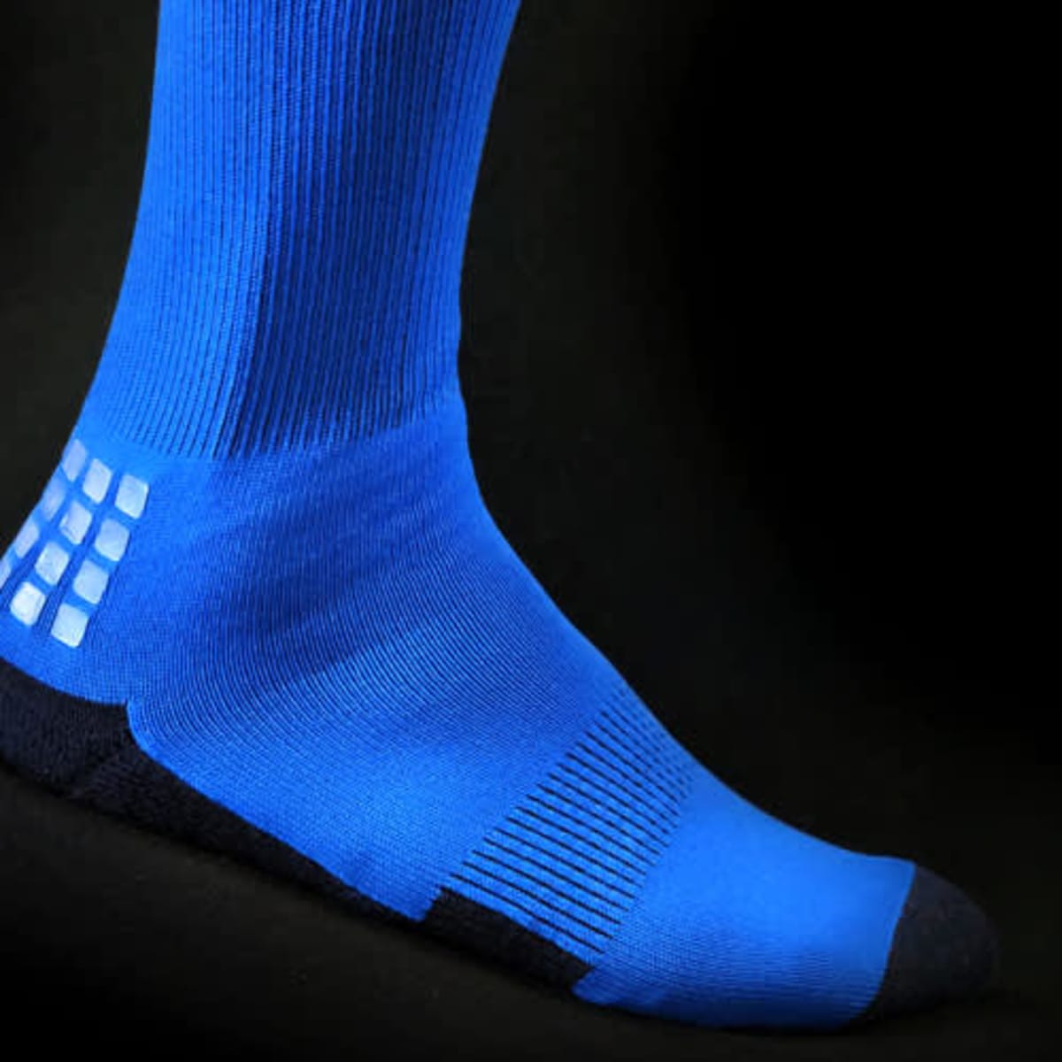 Bright blue athletic socks with a textured grip pattern and a dark blue cuff section, displayed against a black background.