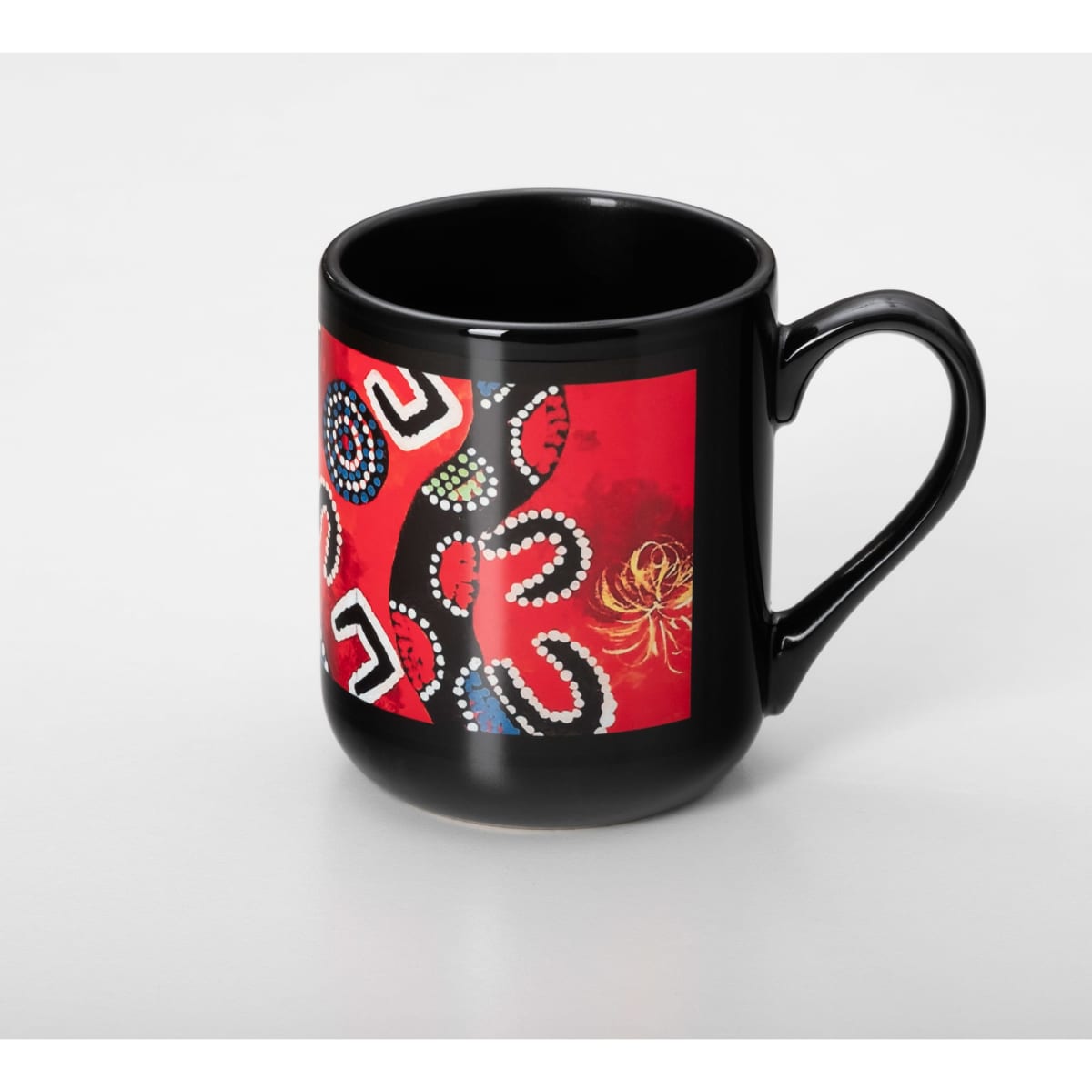 A black coffee mug featuring a vibrant red design with intricate patterns and a logo.