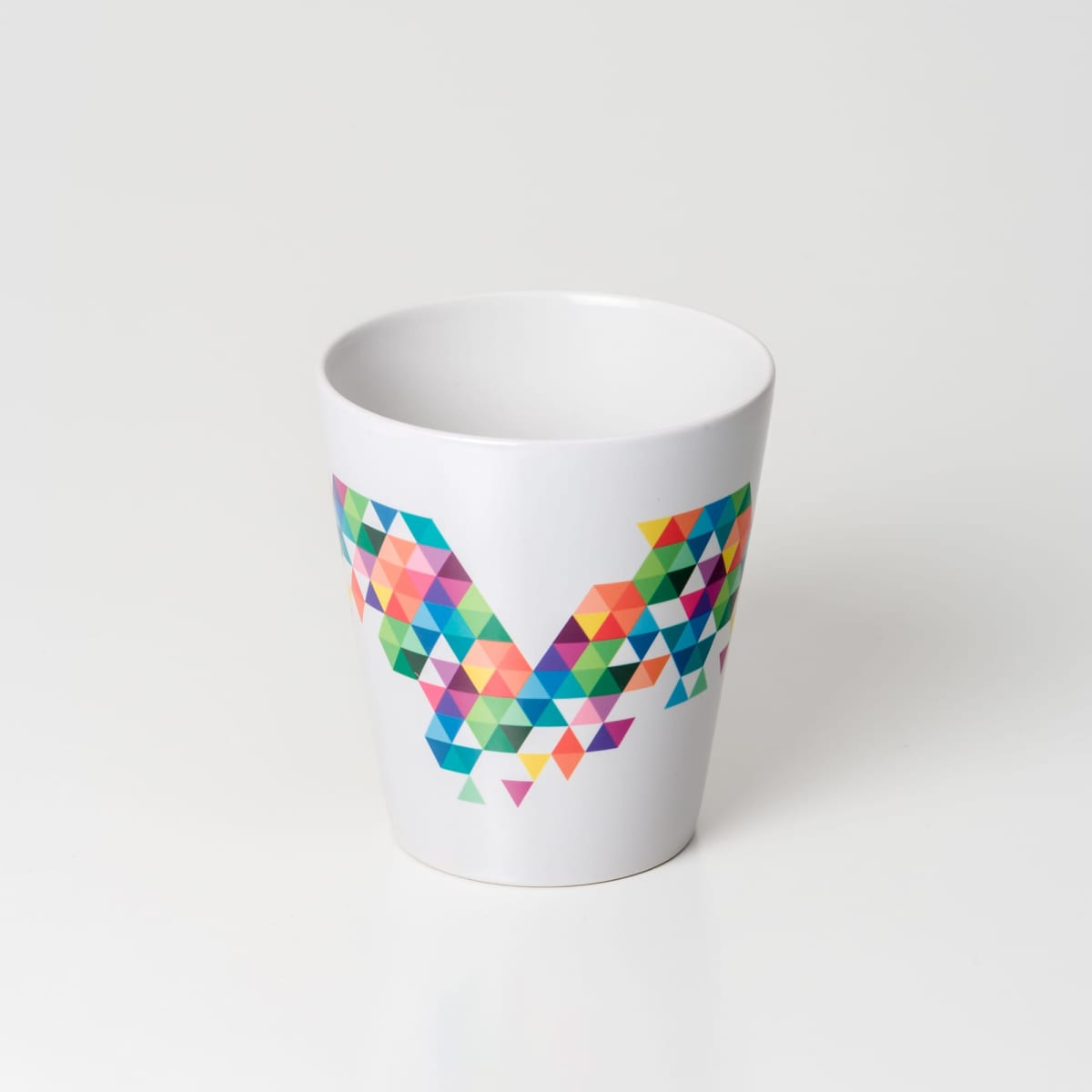 A white coffee mug featuring a vibrant, geometric pattern in various colours, including pink, green, and blue.