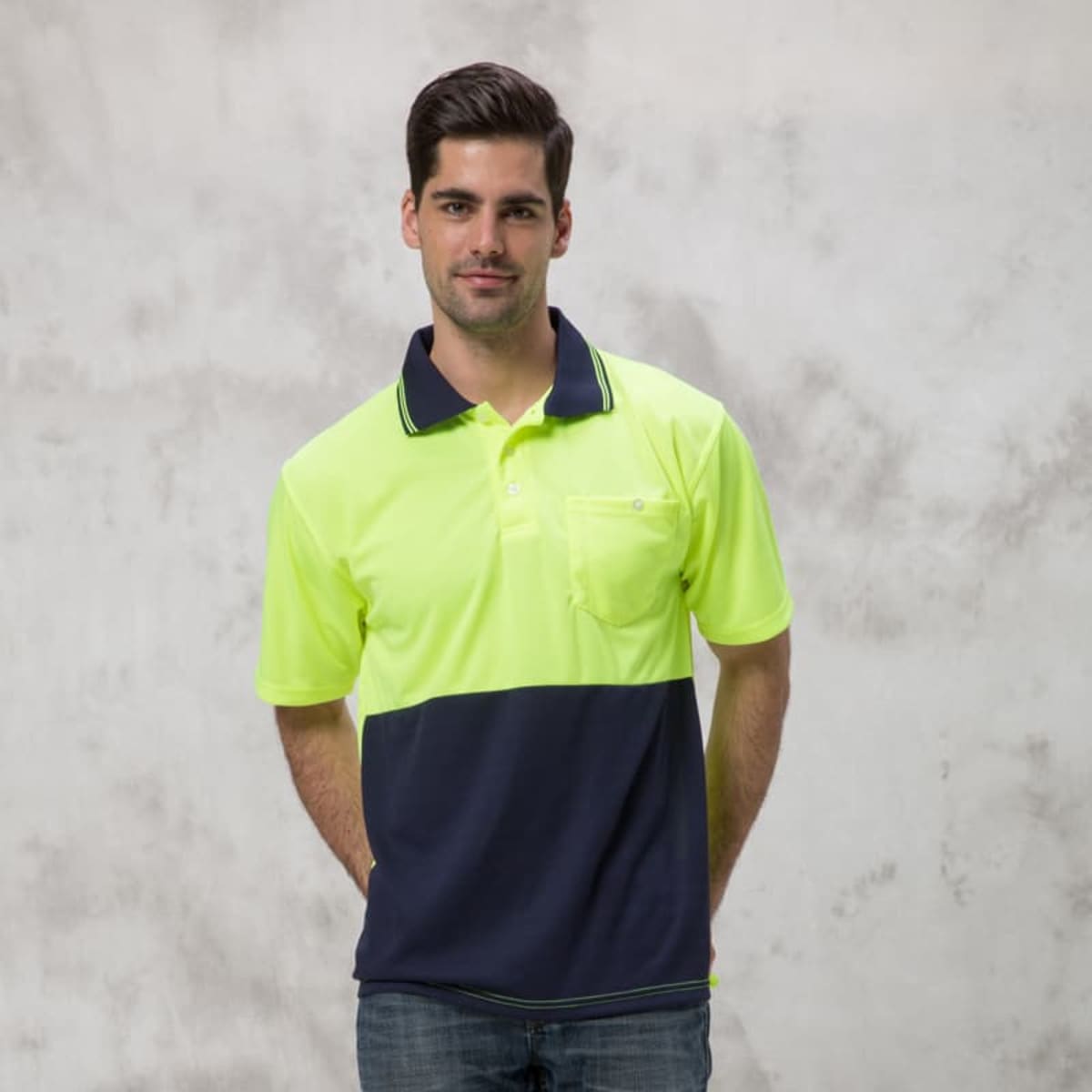 A man is wearing a high-visibility yellow and navy polo shirt with a logo on the chest pocket.