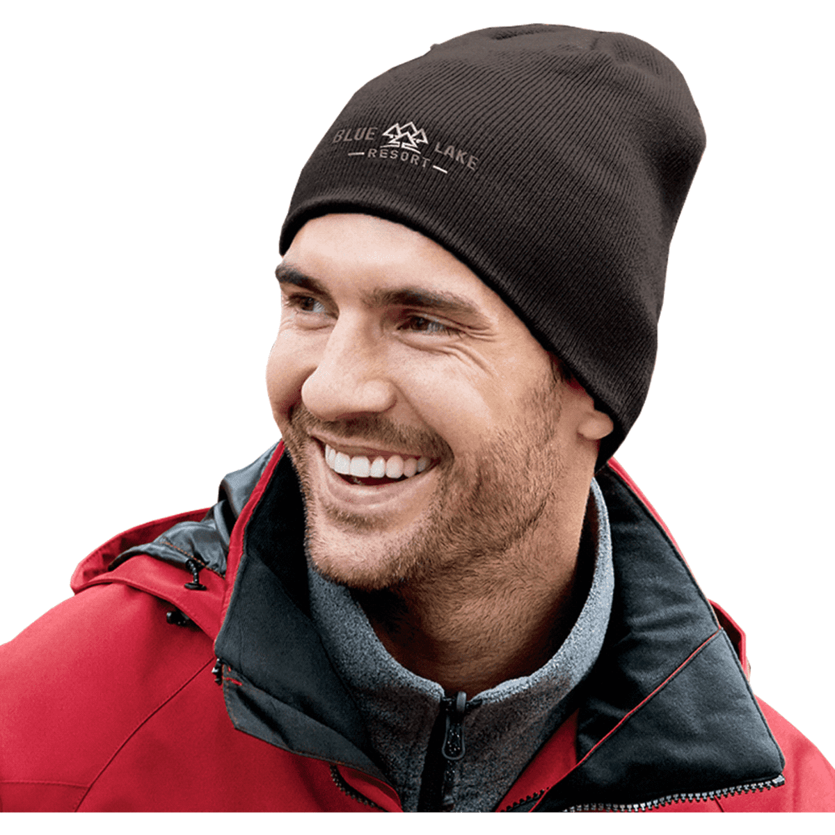 A man wearing a brown knitted beanie smiles, paired with a red jacket and grey sweater, featuring a logo on the beanie.