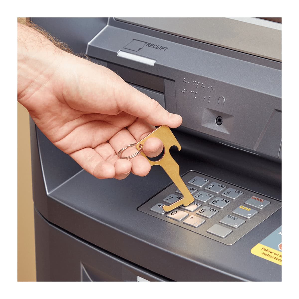 A gold no contact keychain with a keyring is being used at an ATM keypad.