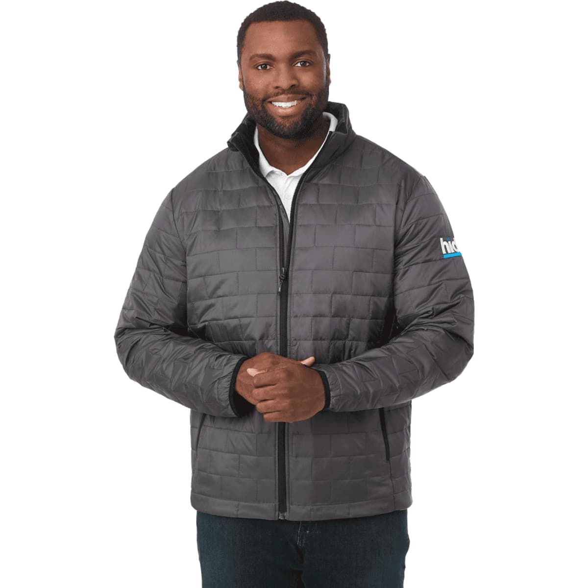 A man wearing a grey puffer jacket with a zip front and a logo on the sleeve.