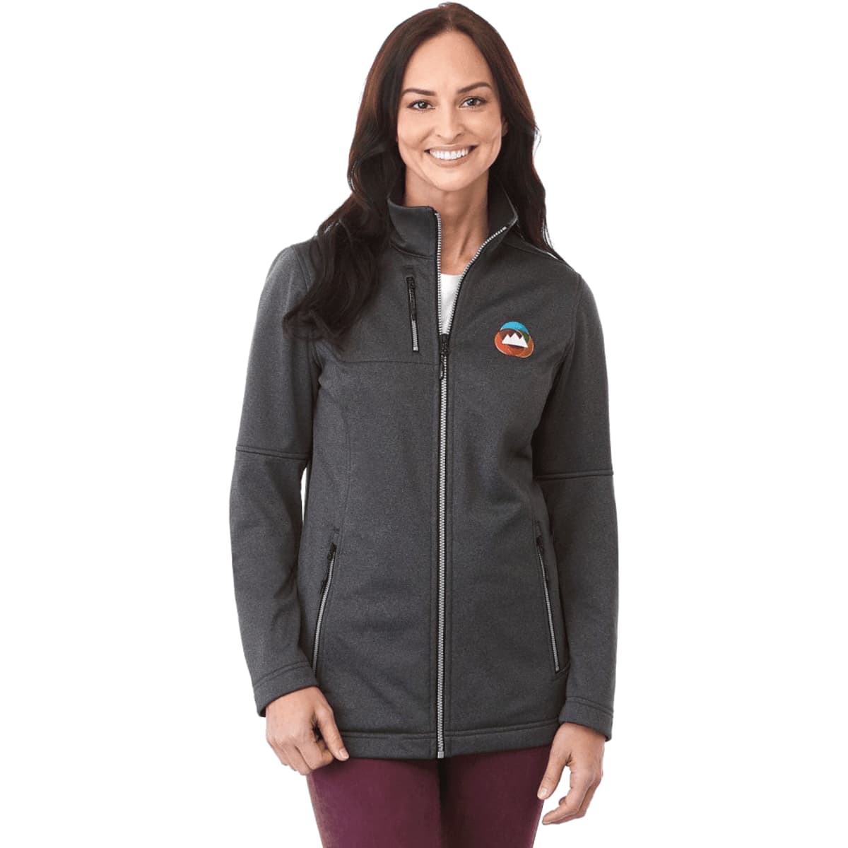 A woman wearing a charcoal grey softshell jacket with a logo on the chest and zippered pockets.