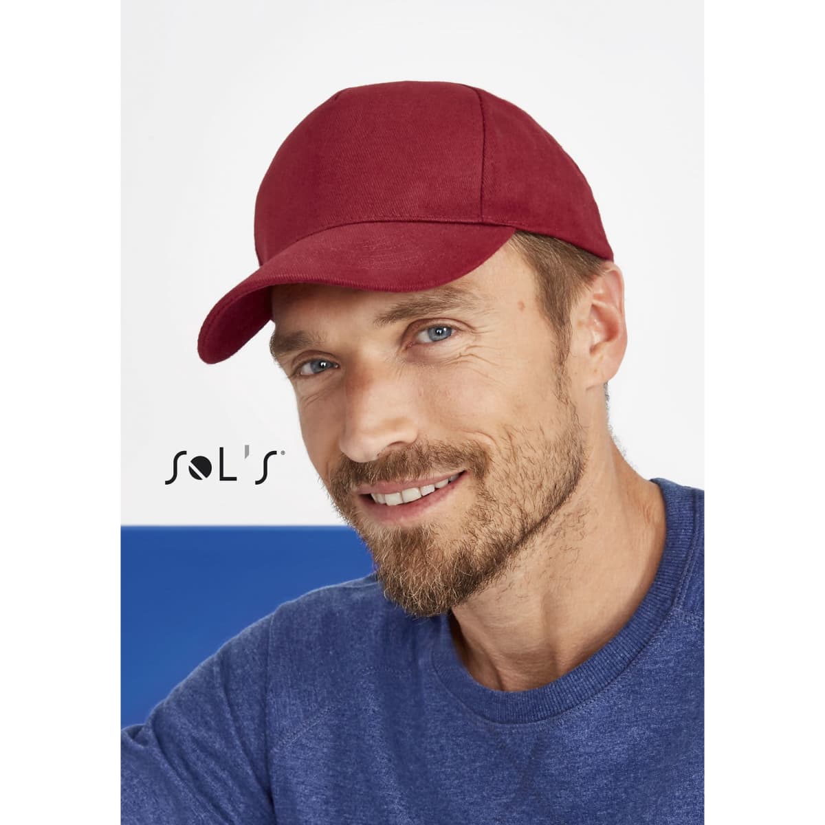 A red five-panel cap made of heavy brushed cotton, featuring a logo. The model has a beard and is smiling.