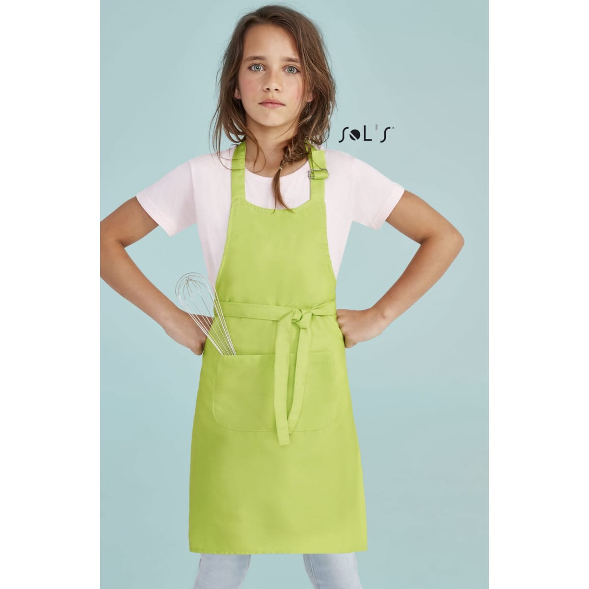 A kids' size apron in bright green with a front pocket, modelled by a girl holding a whisk, on a pastel background.