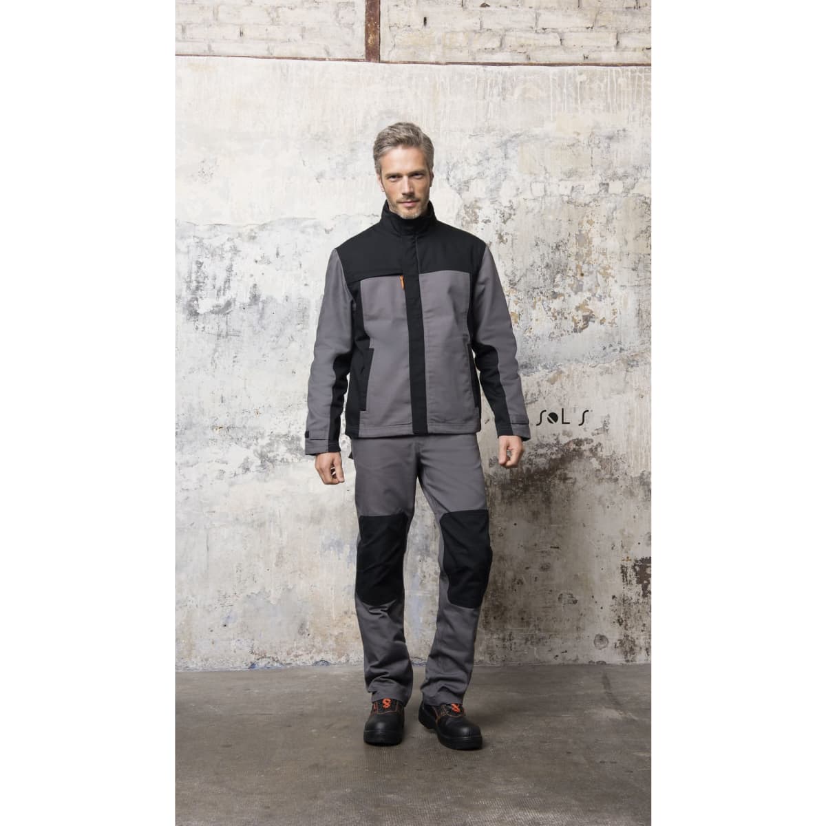 A men's two-colour workwear jacket in grey and black, paired with matching work trousers and black footwear.