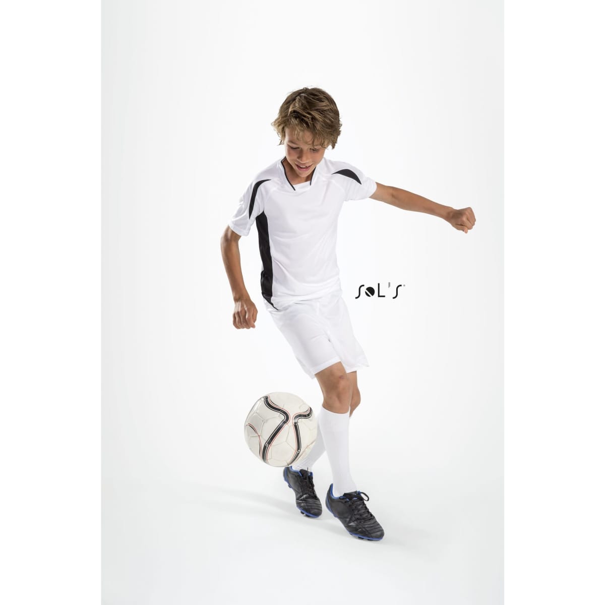 A child wearing a white soccer jersey with black accents, kicking a soccer ball.