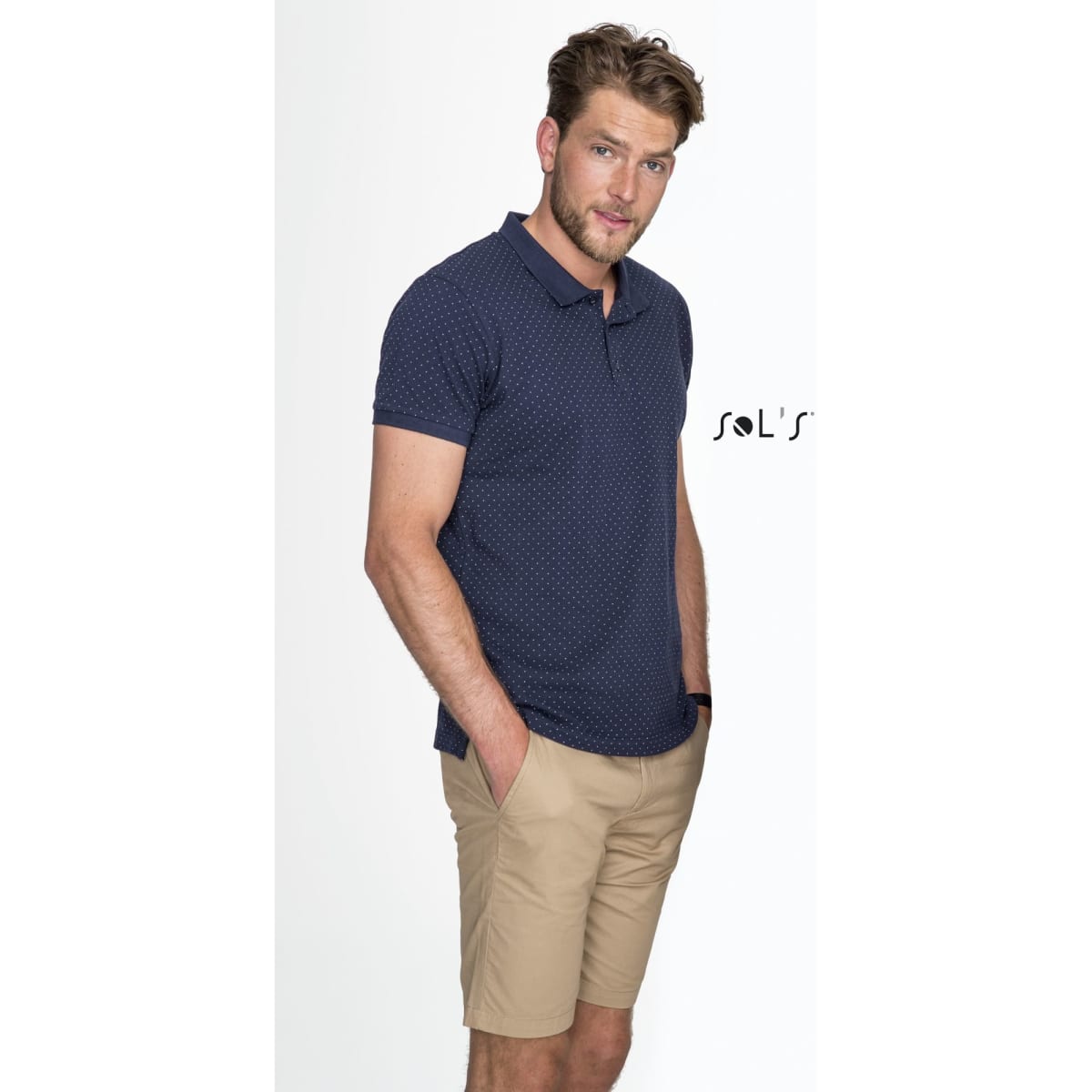 A man models navy blue polo with a pattern and beige chino-style shorts, featuring a logo.
