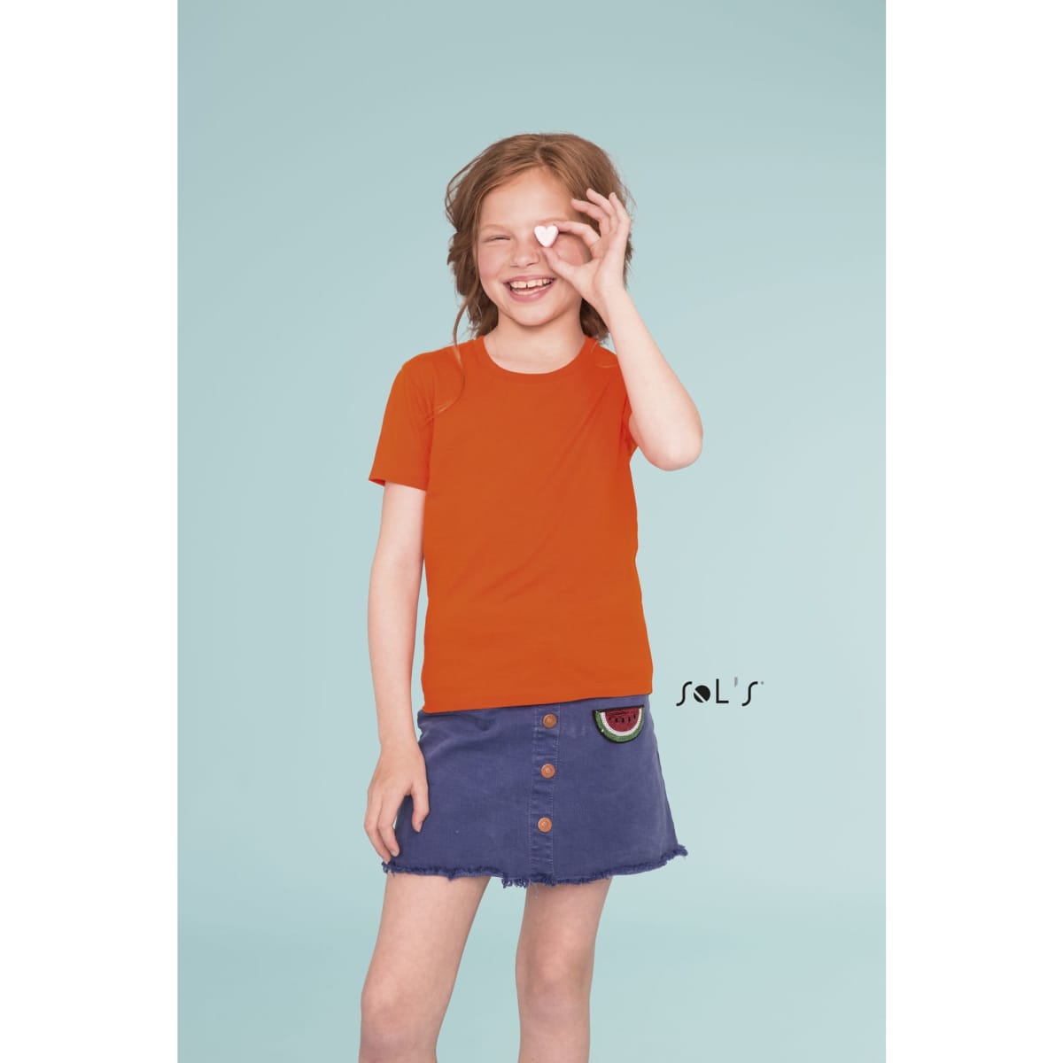 An orange round neck T-shirt made from 100% organically grown cotton, worn by a smiling child. Features a logo.