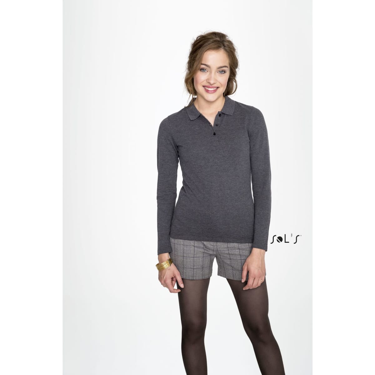 A woman stands in a grey long-sleeve polo shirt made of 100% cotton pique, paired with shorts and tights.