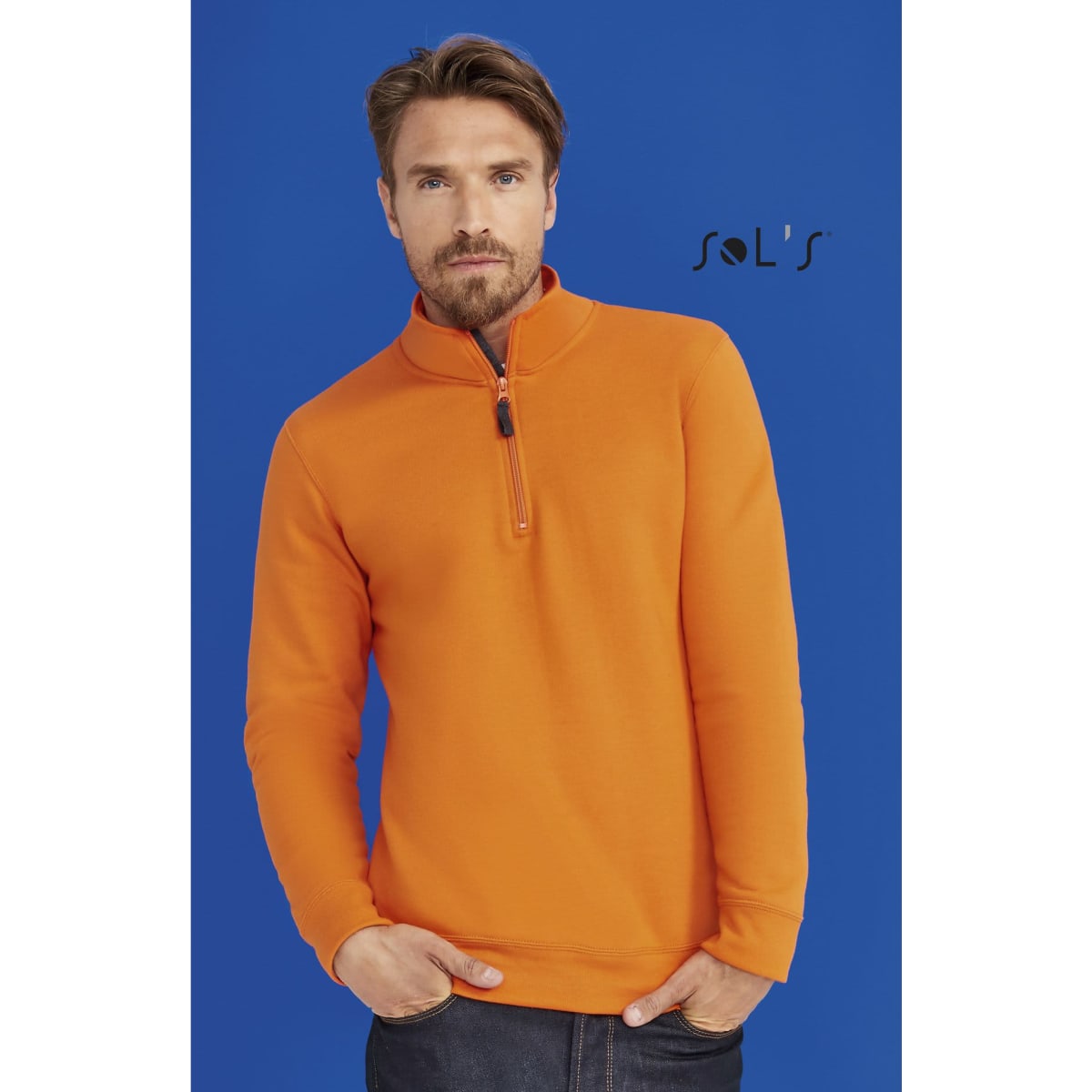 An orange windcheater with a 1/4 zip, worn by a man against a blue background. The garment features a logo.
