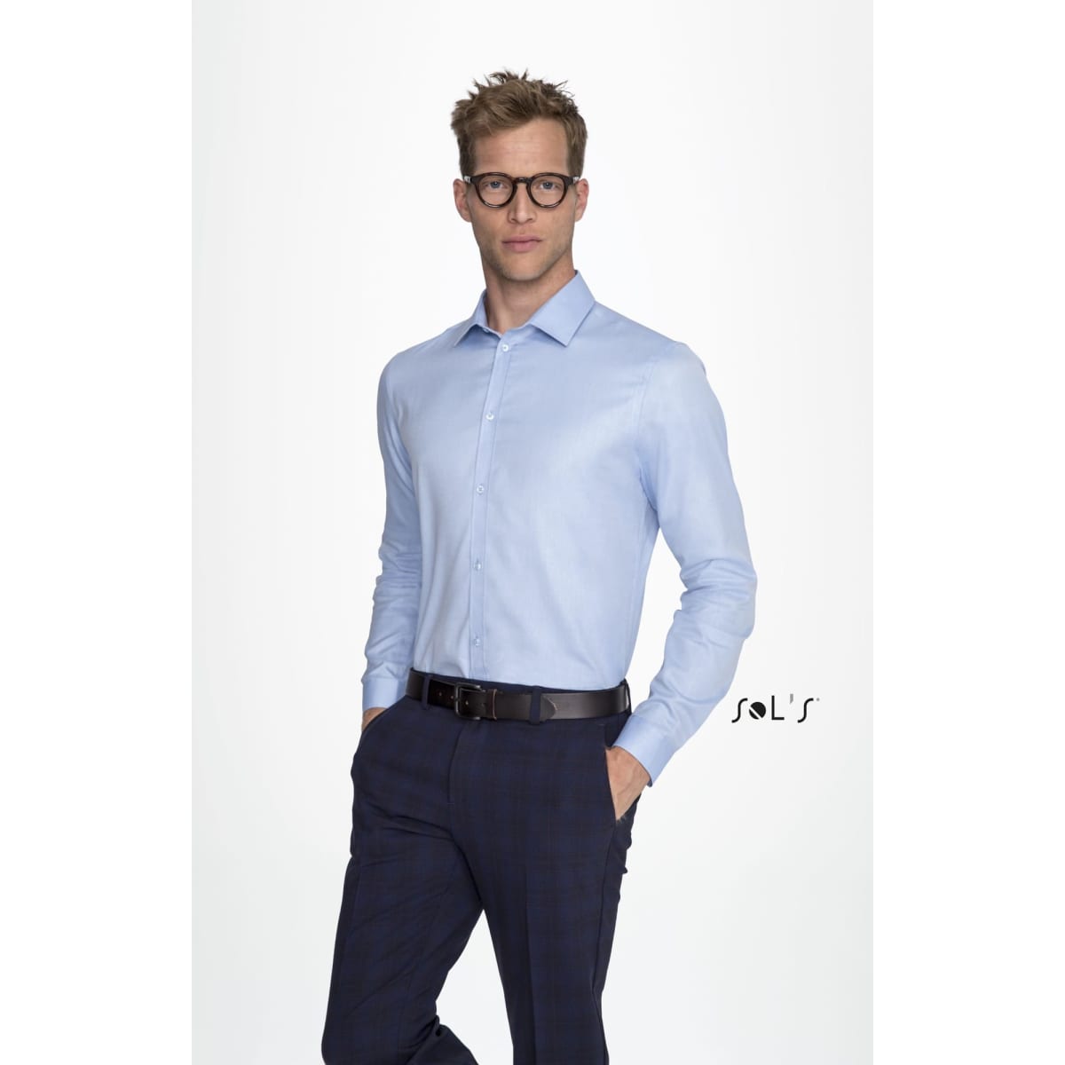 A long-sleeve light blue herringbone shirt worn by a man with glasses, paired with dark trousers. It features a logo.