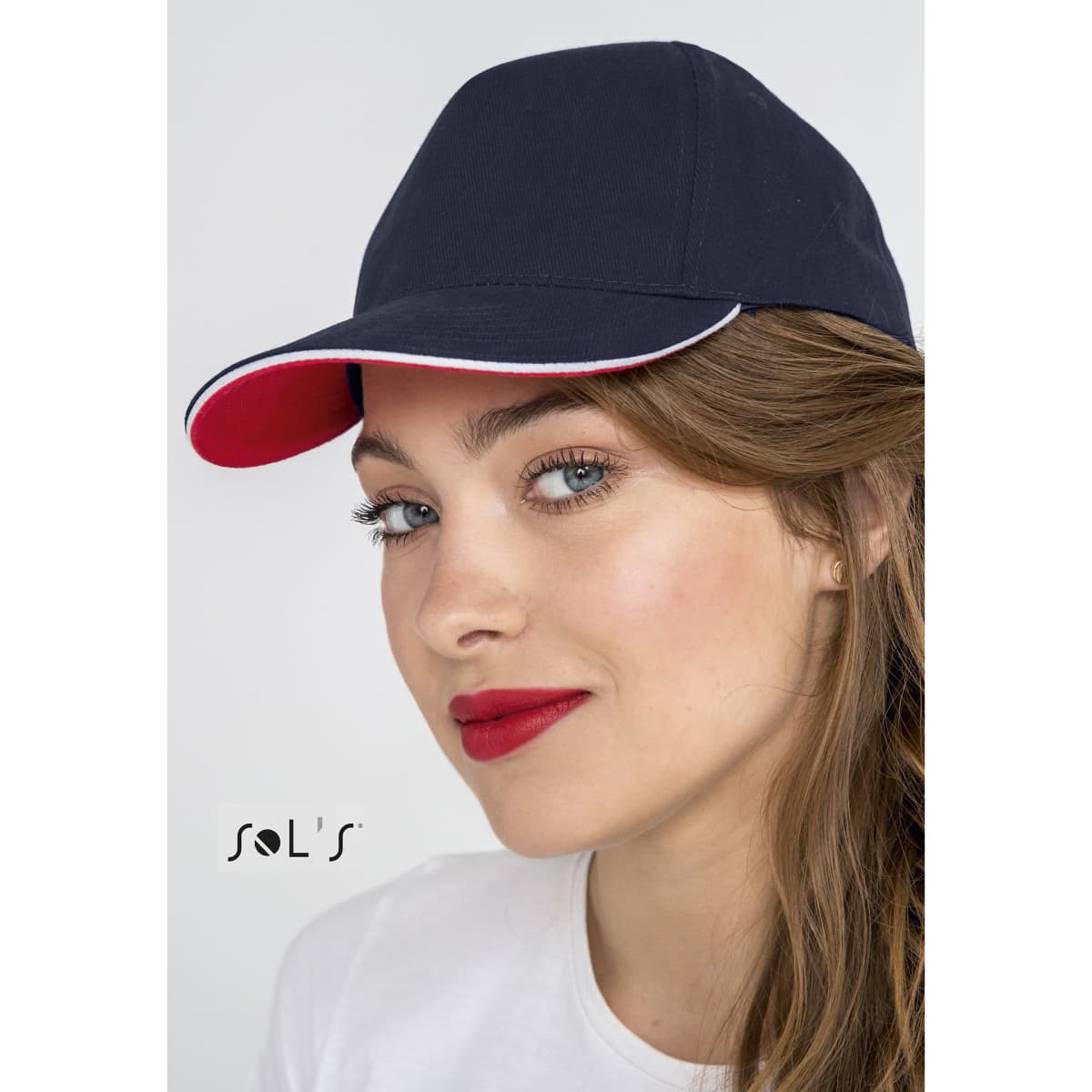 A navy blue cap with a red brim, featuring a logo, displayed on a model with natural makeup.