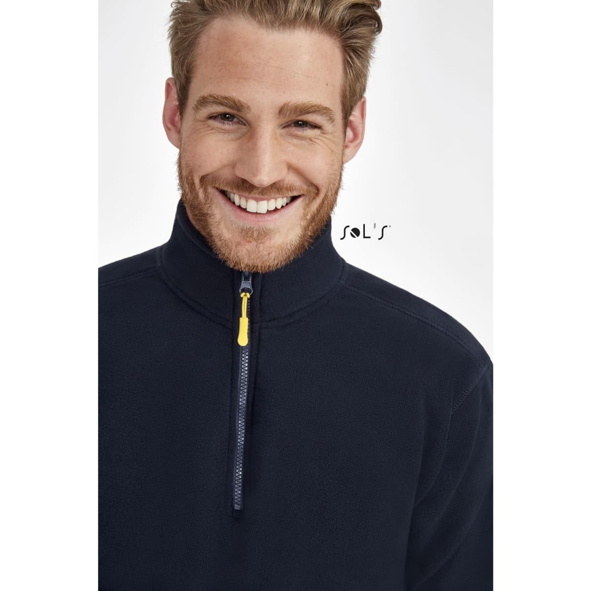 A smiling man wearing a navy blue fleece jacket with a zip and a yellow puller, featuring a logo on the side.